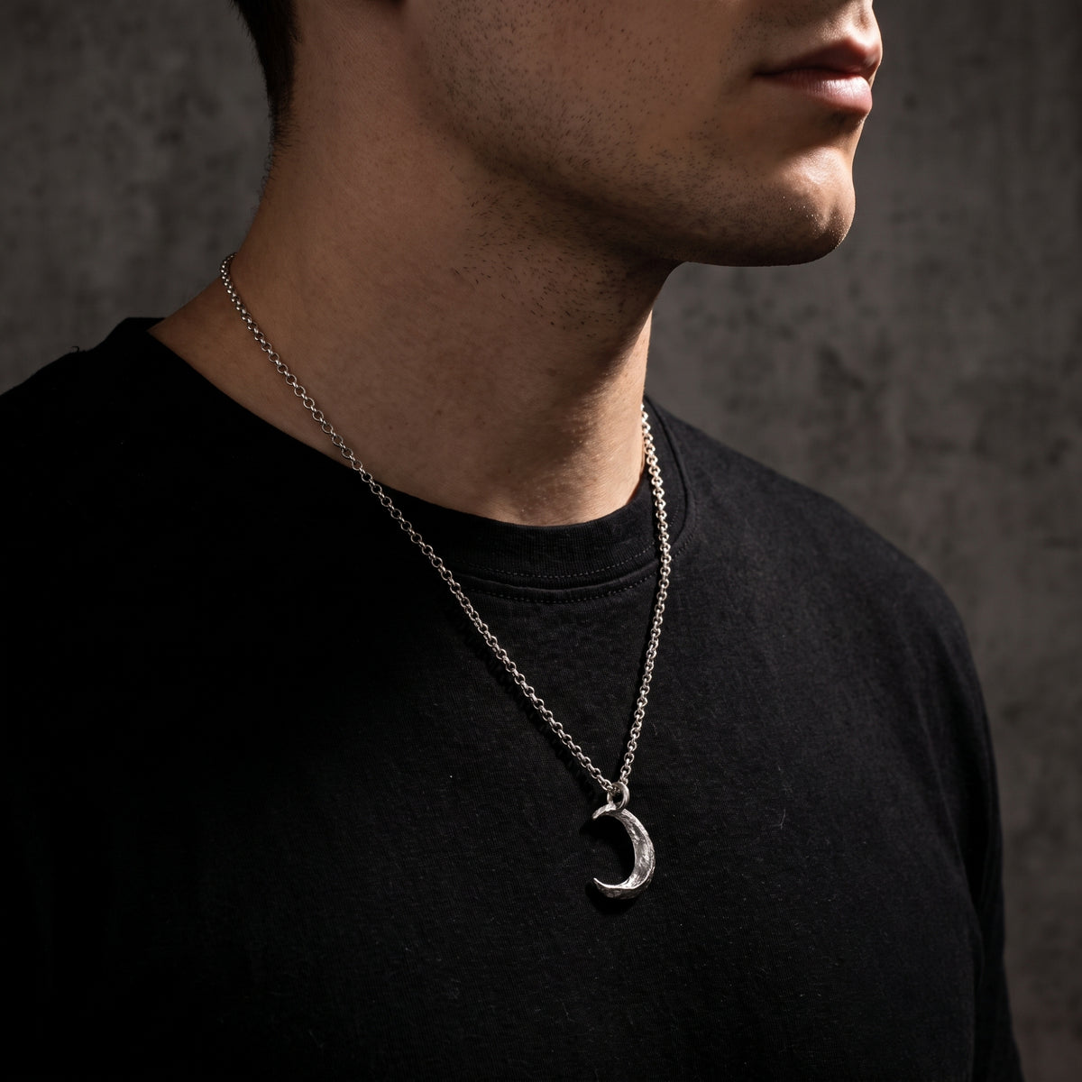 Side profile view of a man wearing the cratered silver crescent moon necklace on a black shirt.