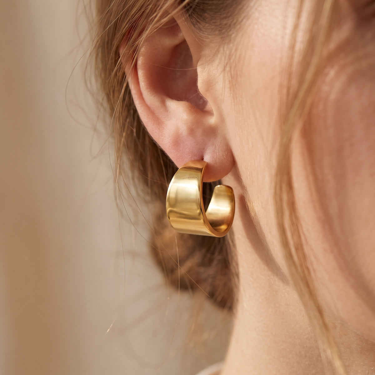 Side close-up of a model wearing one gold-tone flared hoop earring