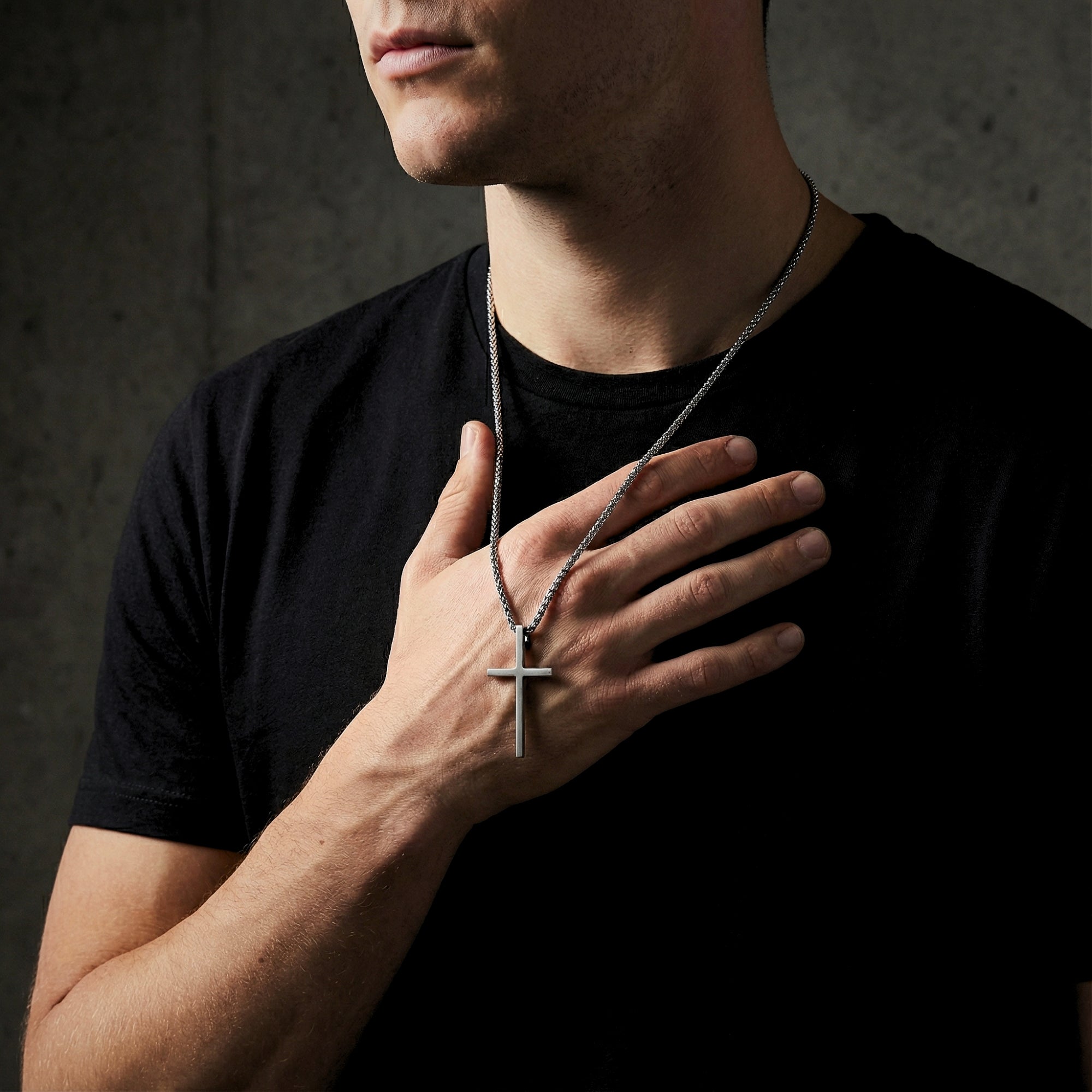 Man wearing the silver stainless steel Devotion Cross necklace, holding the pendant against a black t-shirt.