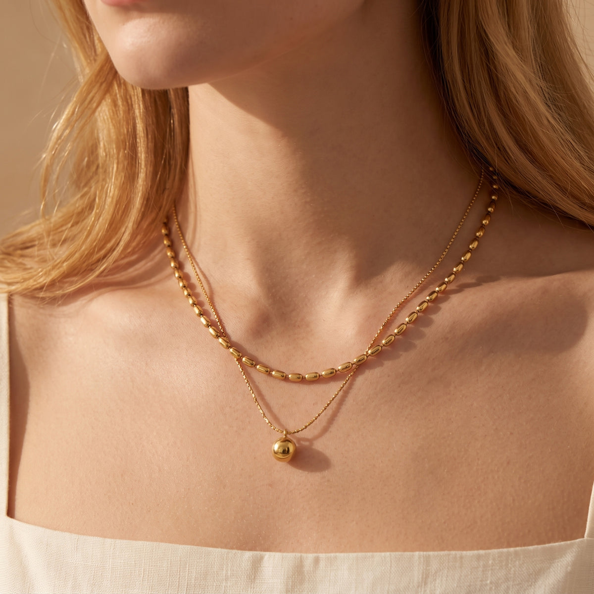 Close-up of a model wearing the gold-toned layered necklace with oval bead strand and sphere pendant.