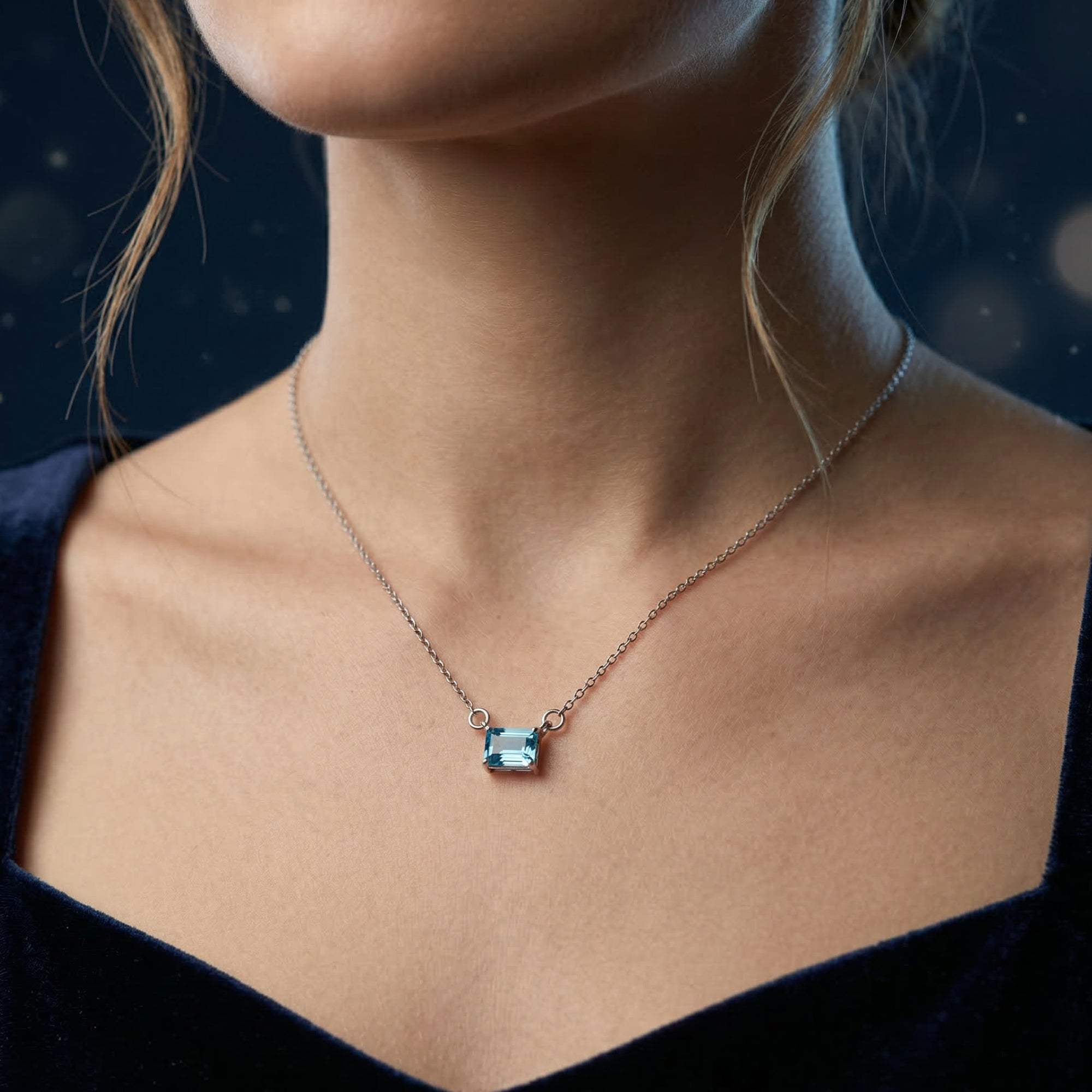 Elyria natural blue topaz necklace in white gold with an emerald cut stone worn by a model.