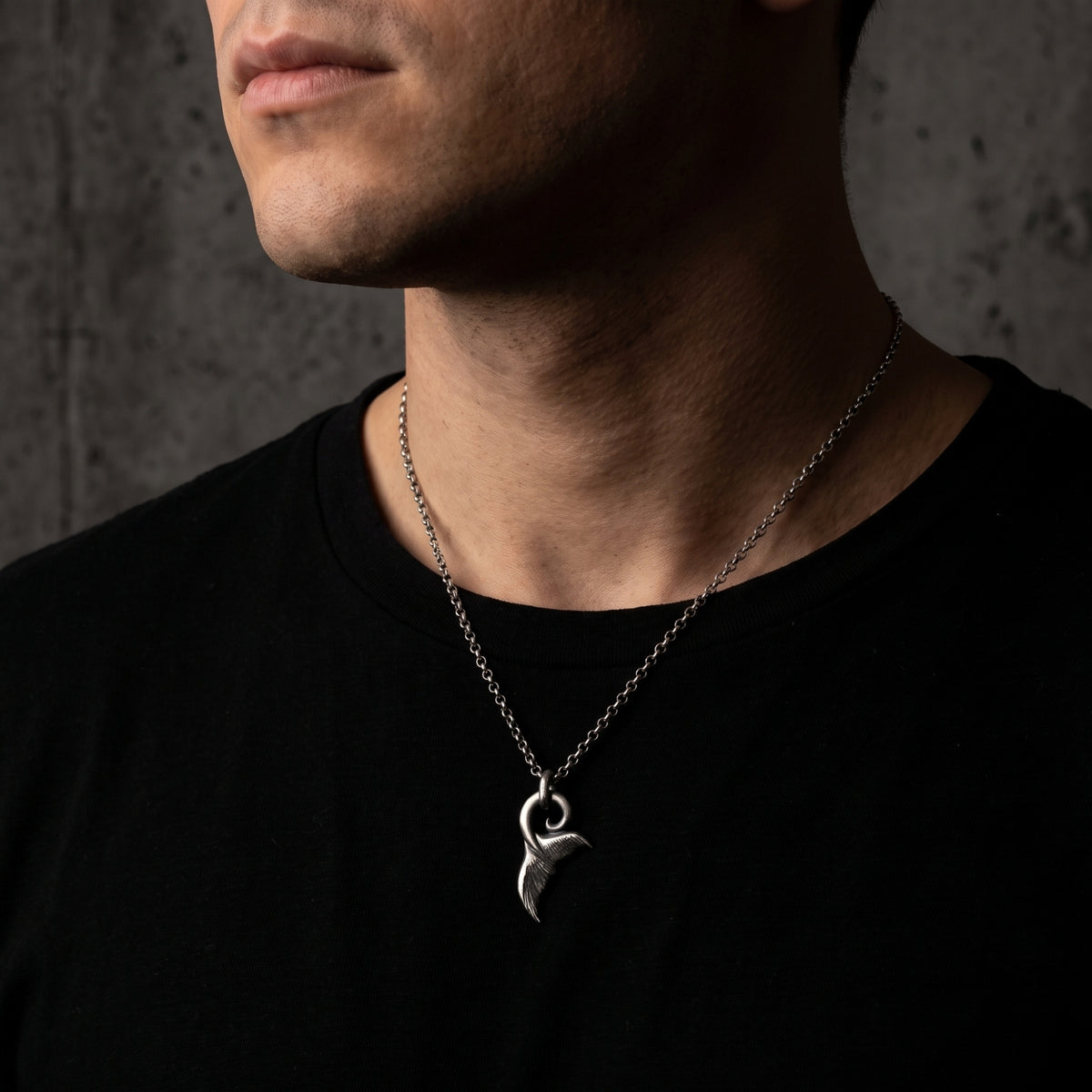 Close-up of a man wearing the silver whale tail fluke pendant over a black T-shirt.