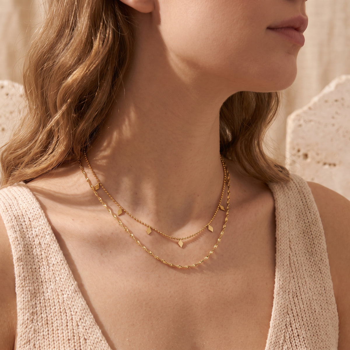 Side view of a woman wearing a gold-tone double-strand necklace with geometric charm stations.