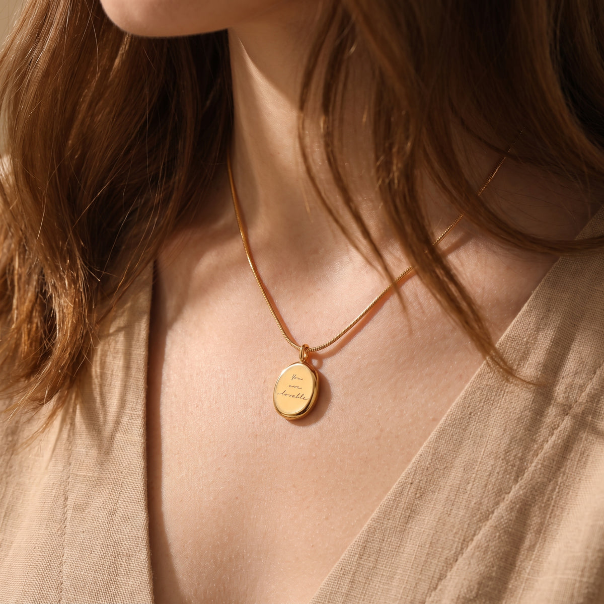 Close-up of a woman wearing the gold-tone oval medallion necklace with “You are lovable” script.