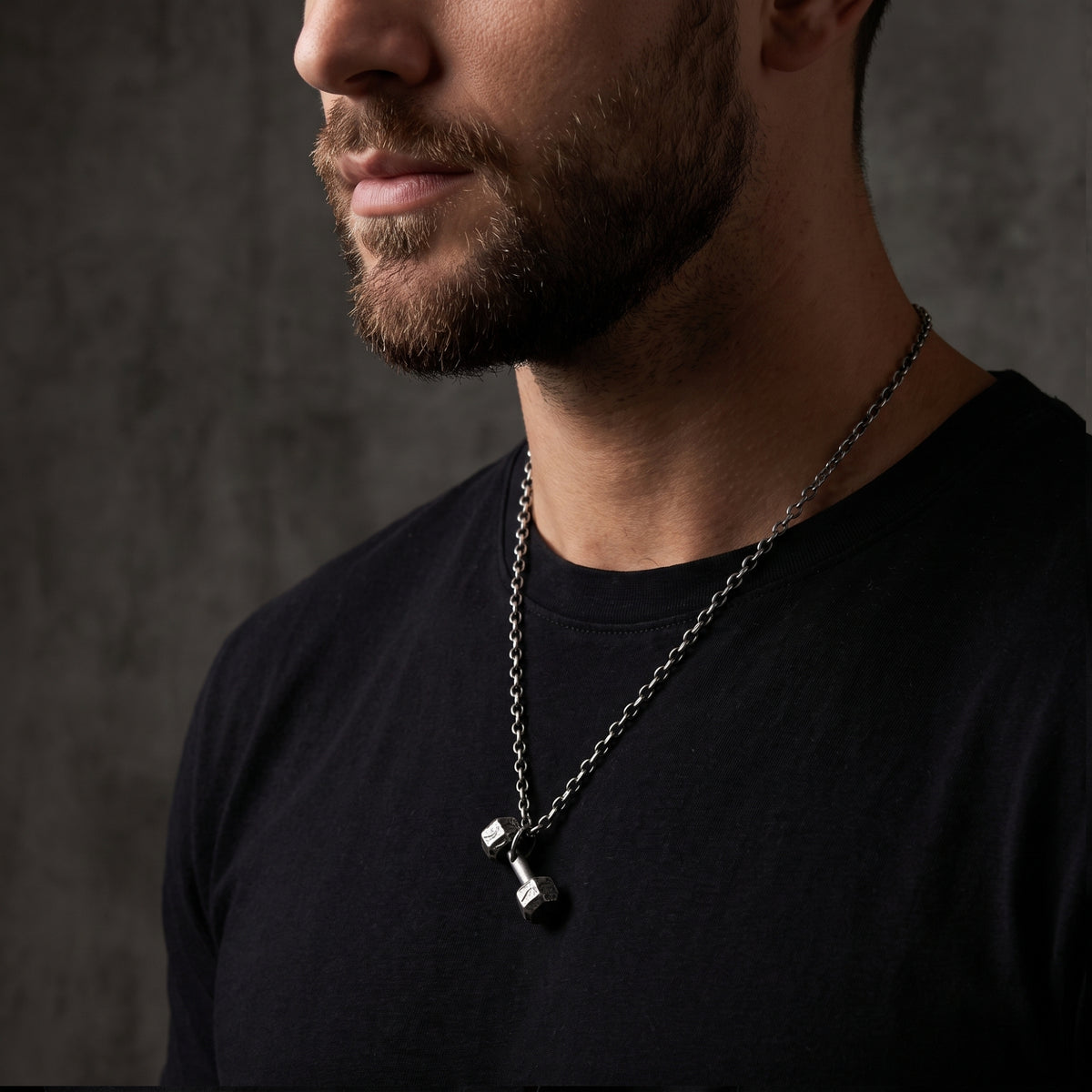 Bearded man wearing a fine silver dumbbell pendant necklace over a black T-shirt.
