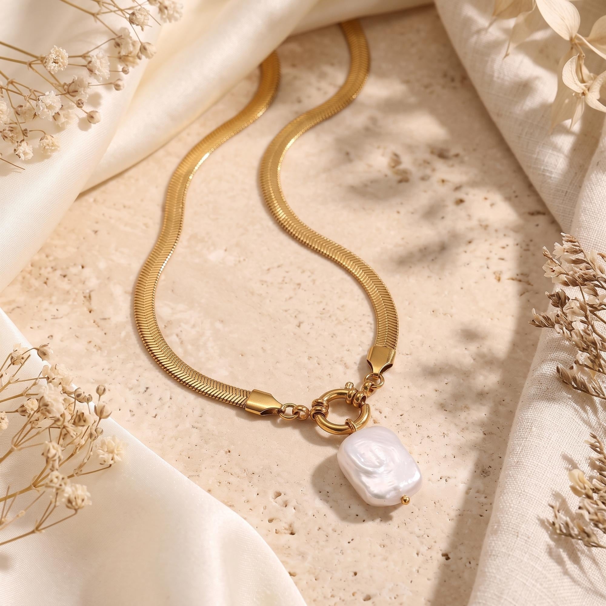 18K gold finish herringbone snake chain necklace with a natural white baroque pearl pendant in a styled scene.