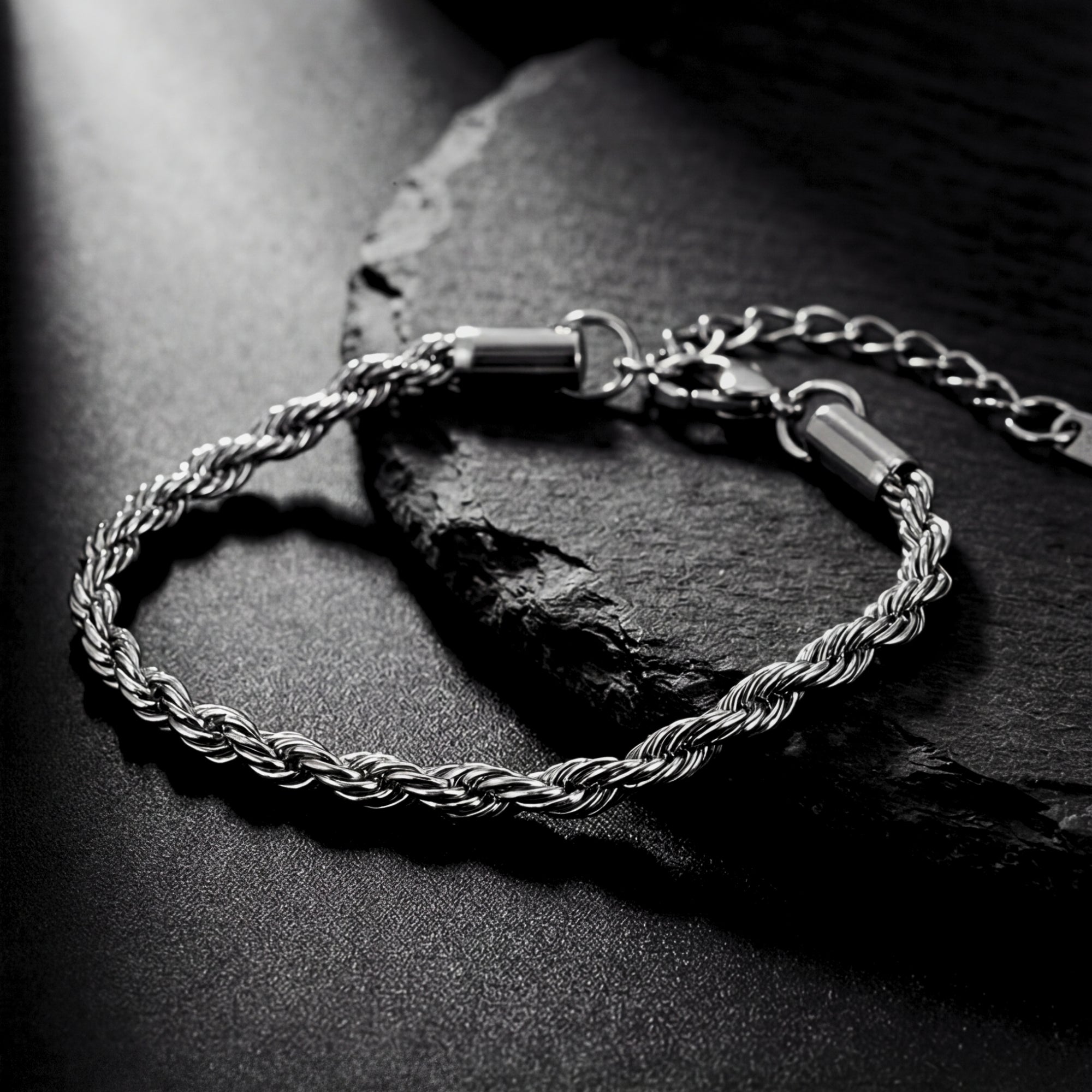 Top view of a silver stainless steel rope chain bracelet for men on a dark slate background.