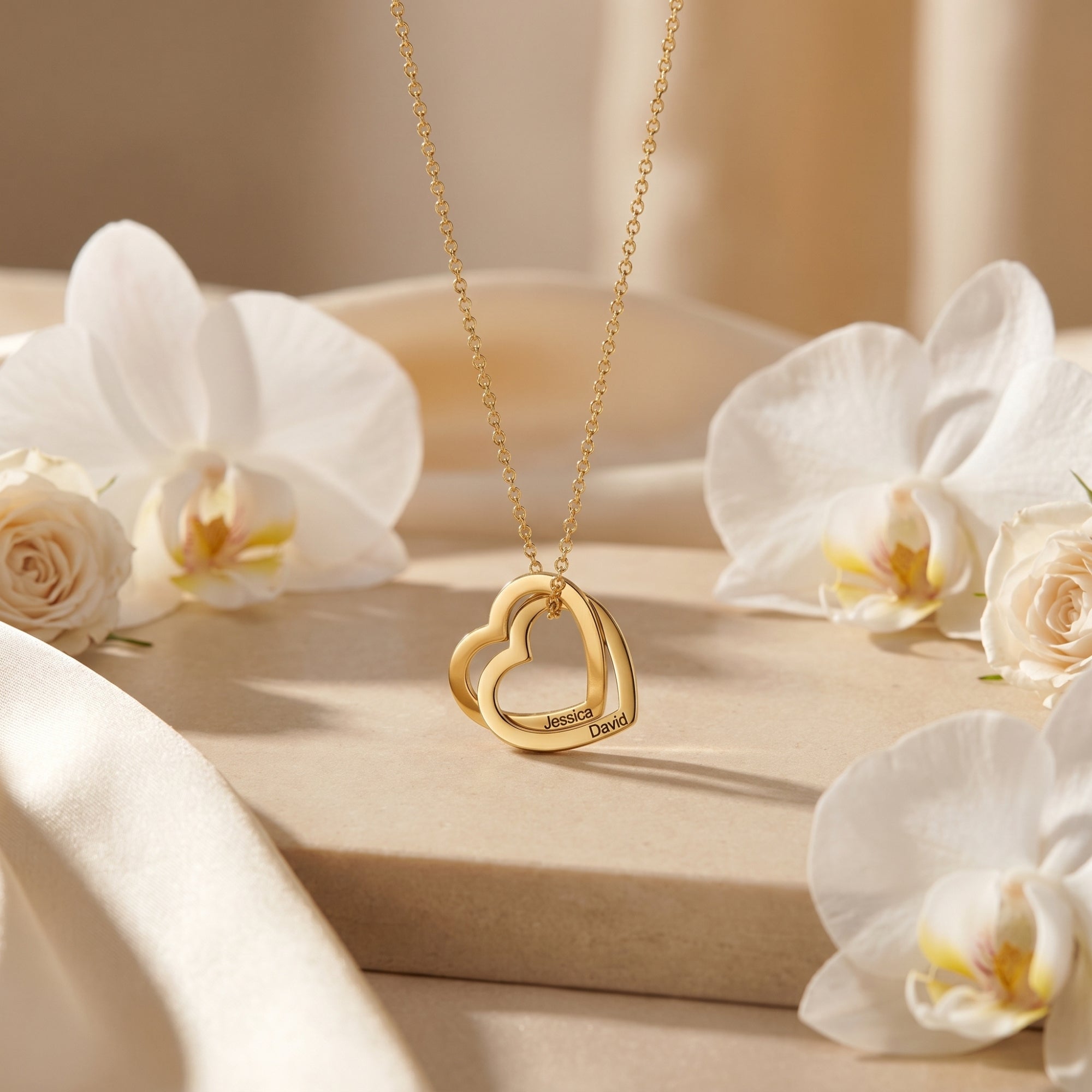 Close-up of the gold interlocking heart pendant with personalized names, styled with white orchids.