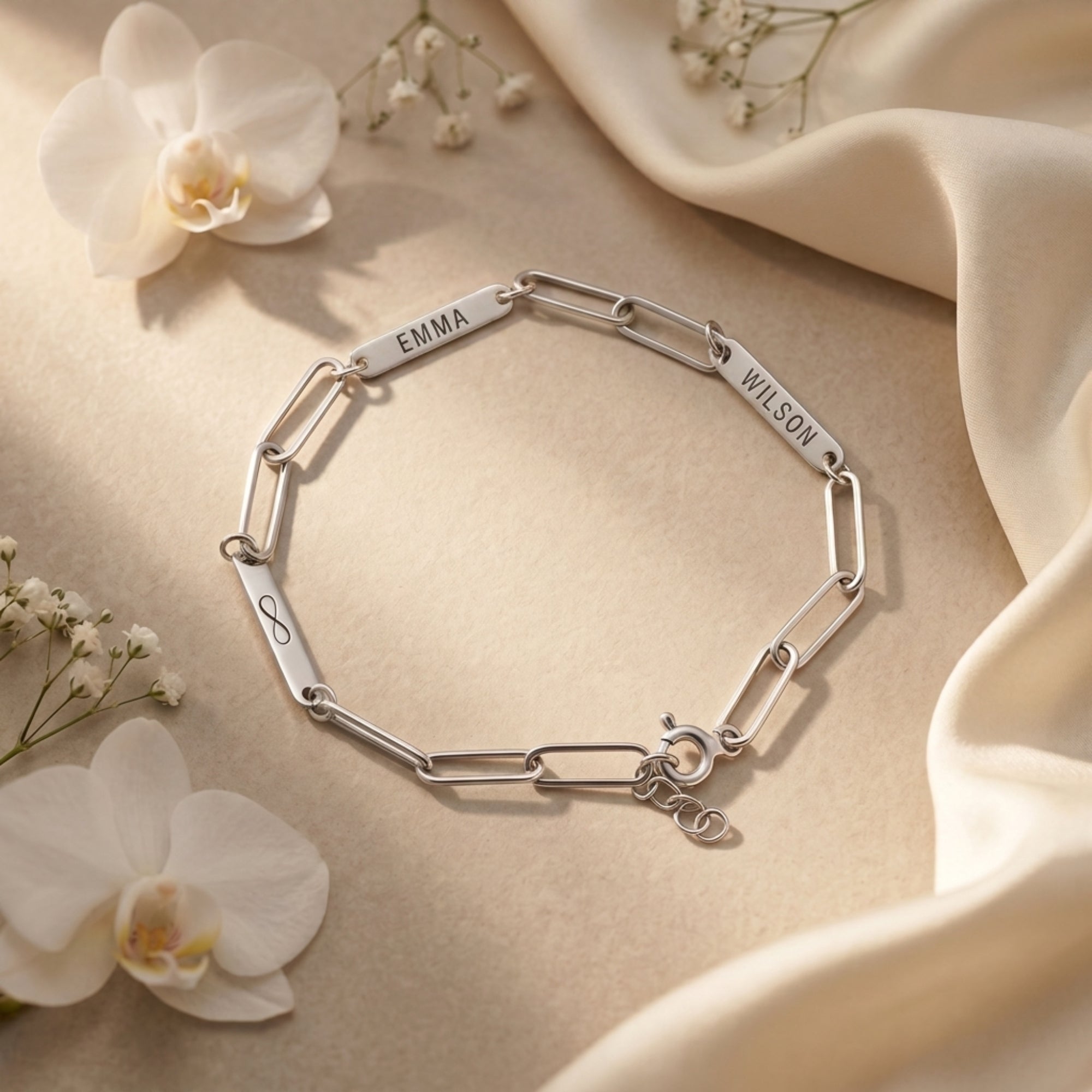 Silver personalized link bracelet with engraved name plates and infinity symbol on a stone surface.