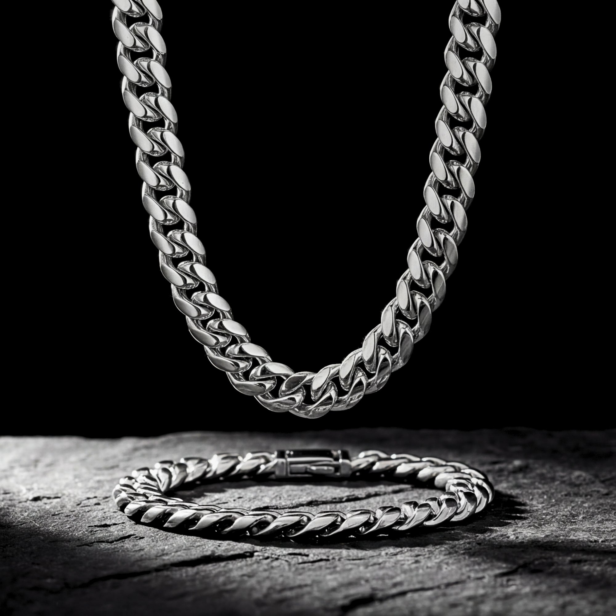 Polished silver 10mm Cuban link chain hanging above a matching bracelet on a dark stone background.