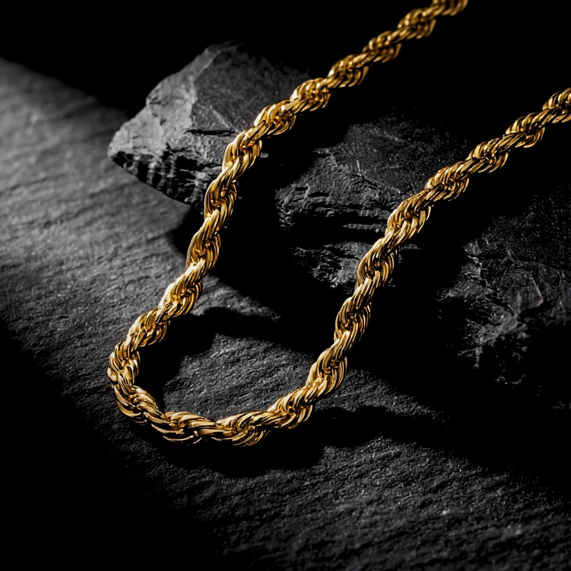 Macro detail of the twisted links on a 4mm gold stainless steel rope chain resting on black stone.