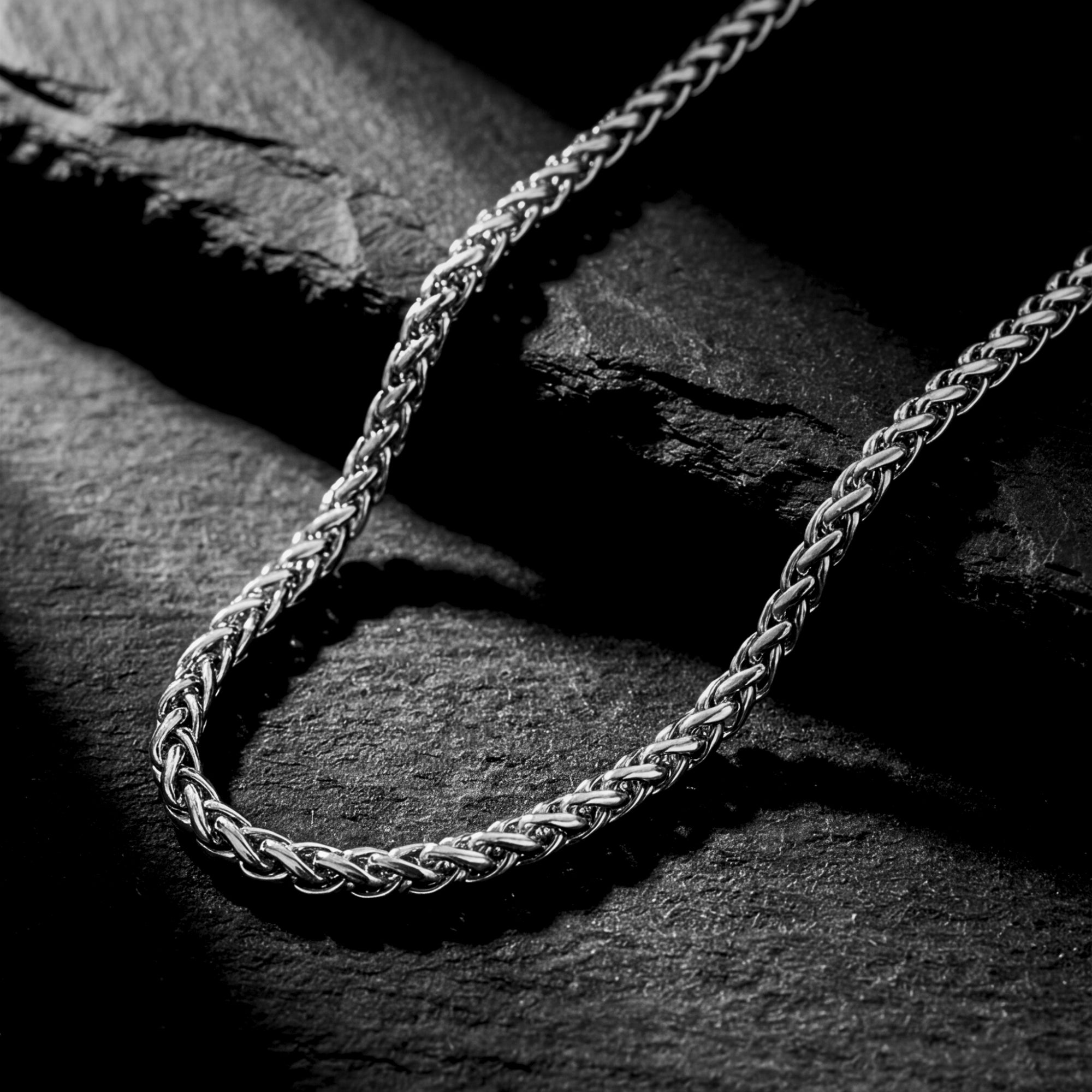 Macro view of the 6mm silver stainless steel wheat chain links on a dark textured surface.