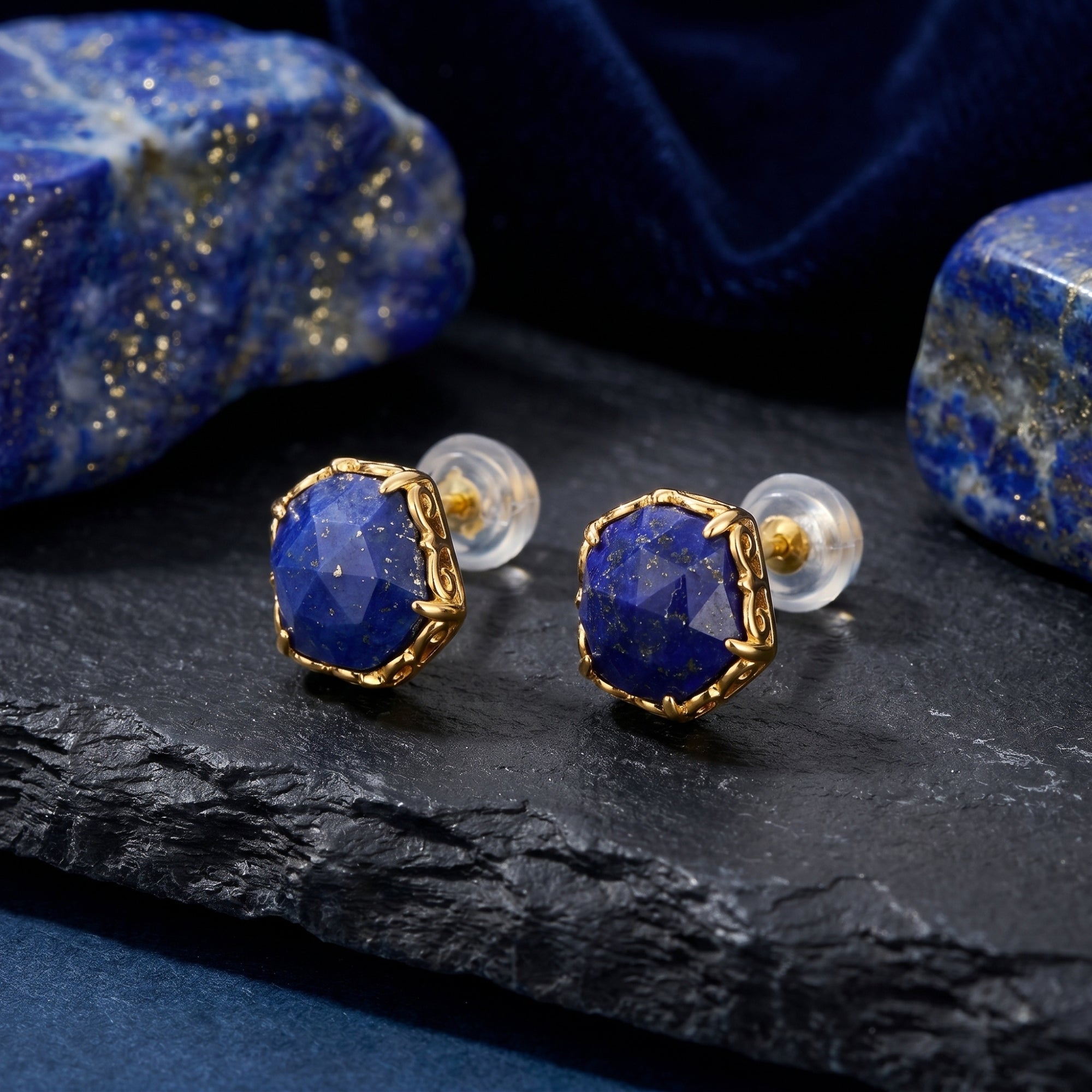 Detail view of gold hexagon lapis lazuli stud earrings with clear silicone backings on a textured stone surface.