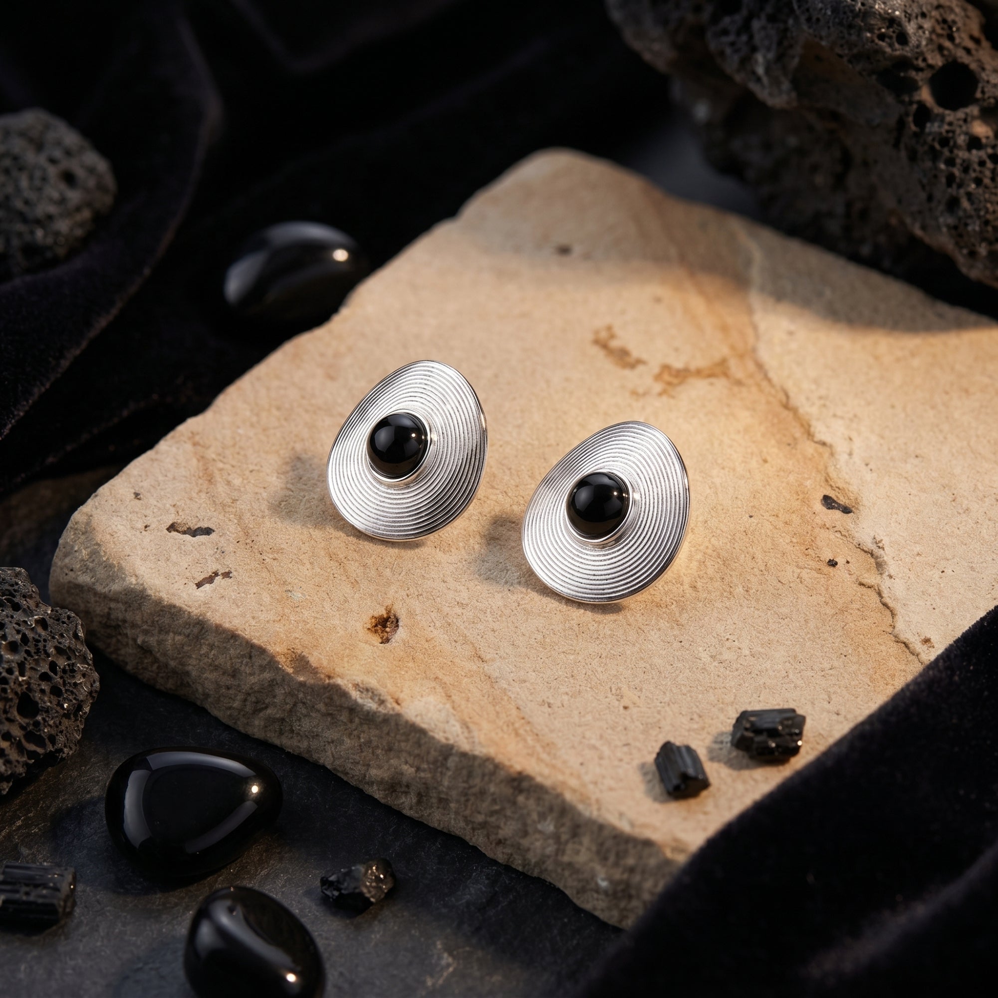 Pair of silver Architect onyx stud earrings displayed on a textured stone slab with black velvet accents.