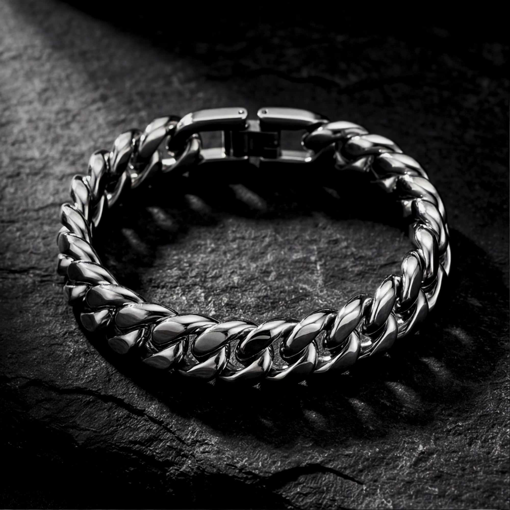 Top view of a silver 12mm stainless steel Cuban link bracelet on a dark stone background.