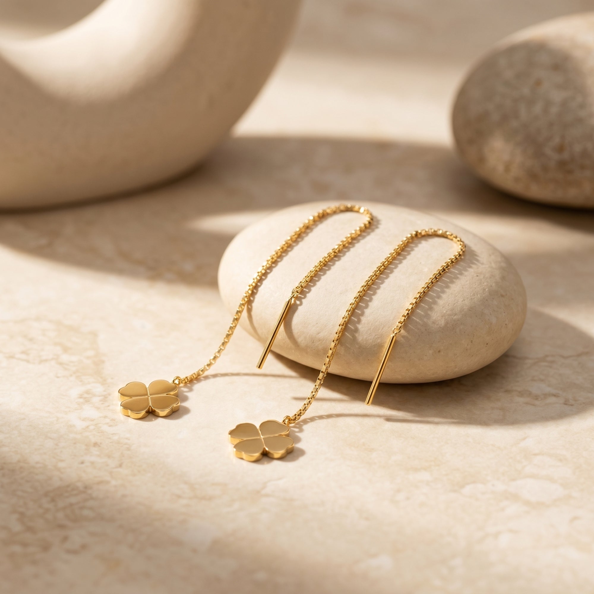 Close-up of 18K gold finish clover threader earrings on a pebble, highlighting the fine chain detail.