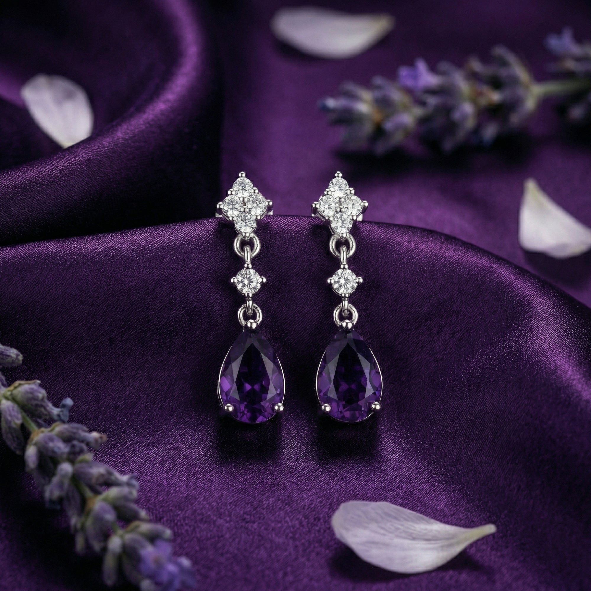 Pair of sterling silver drop earrings with pear cut natural amethyst stones resting on purple fabric.