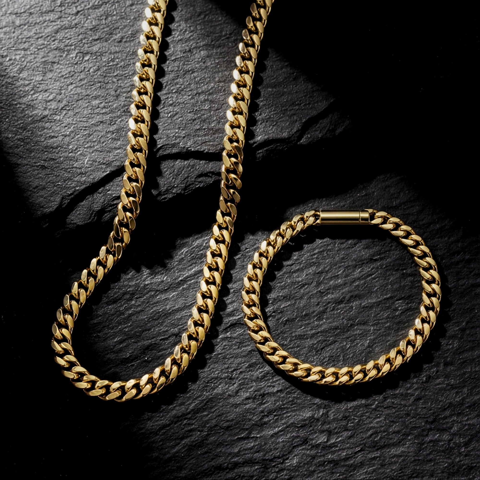 Matching 6mm gold stainless steel Cuban link chain and bracelet set laid flat on a dark stone background.