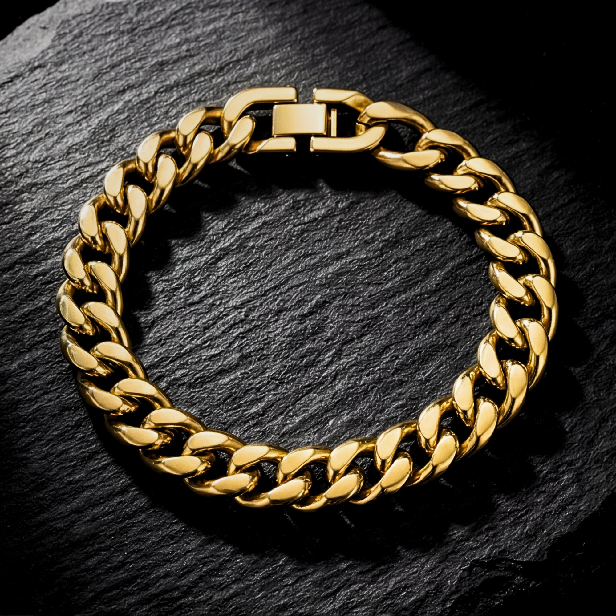 Top-down view of a gold stainless steel Cuban link bracelet resting on a dark slate background.