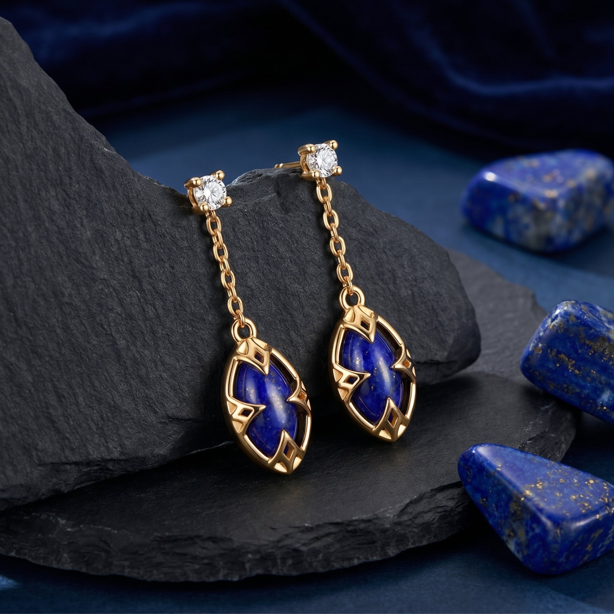 18k gold plated marquise lapis lazuli drop earrings resting on a black slate rock with raw lapis stones.