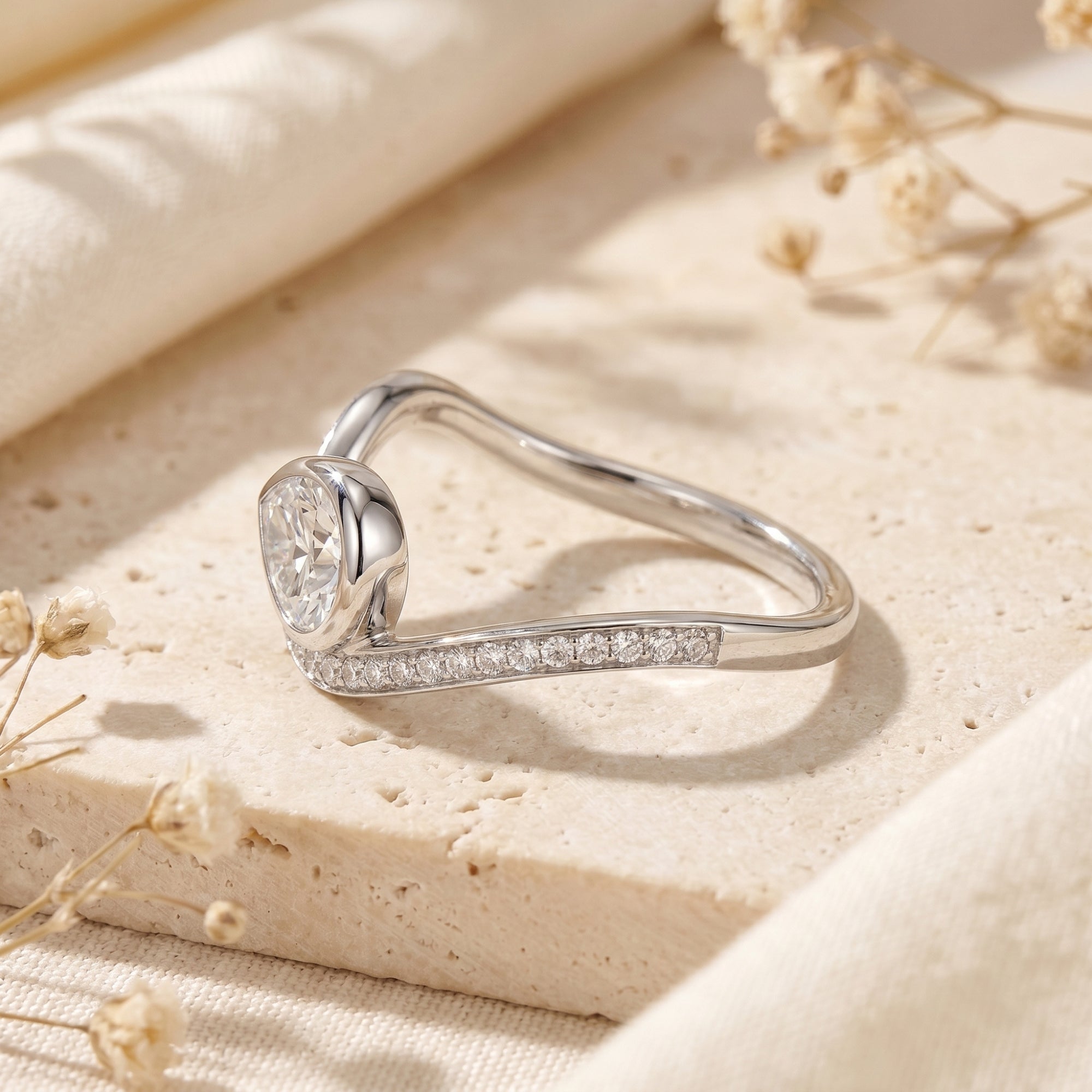 Profile view of silver bypass ring showing bezel-set pear moissanite.