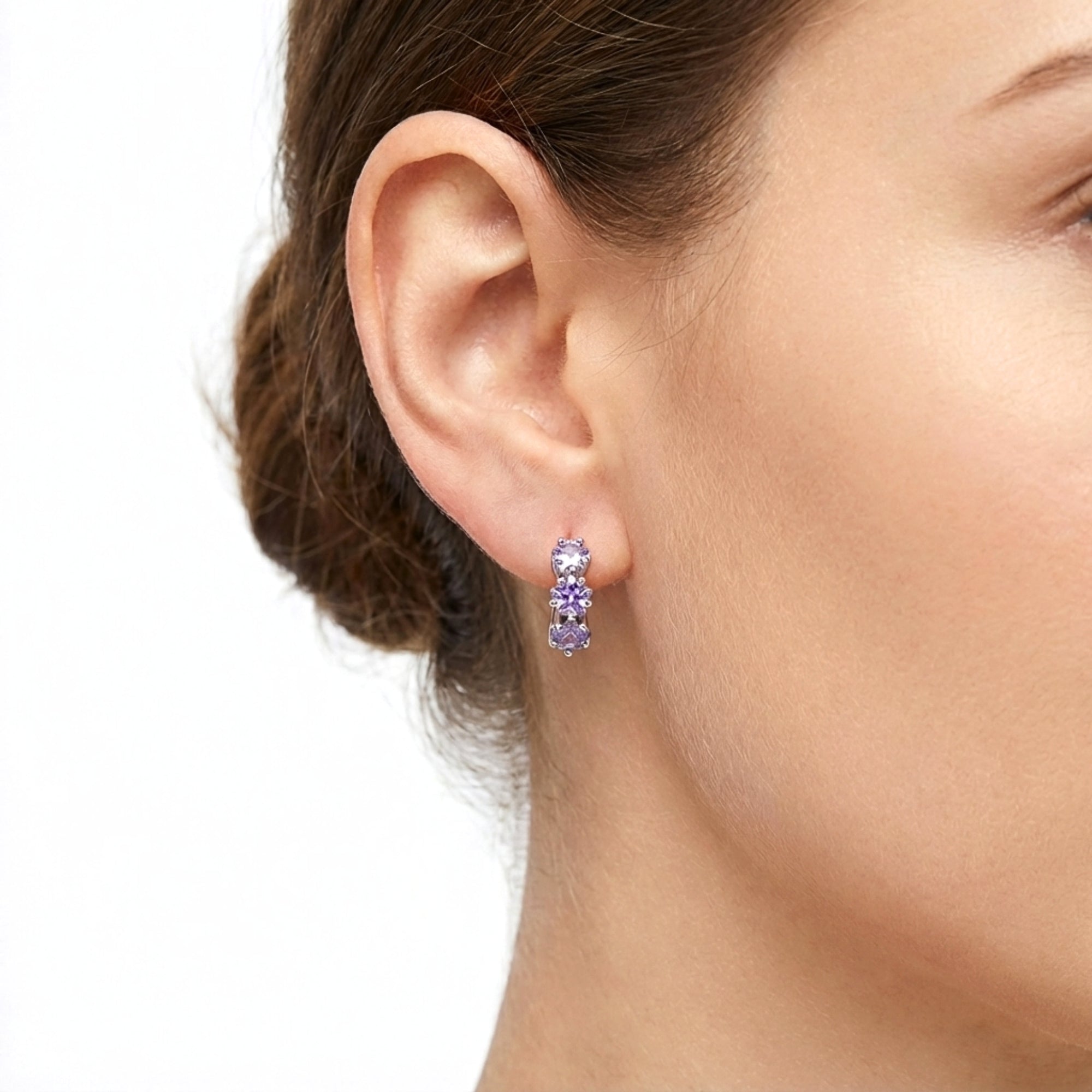 Close-up of a woman wearing a triple-star simulated amethyst huggie earring in S925 sterling silver.