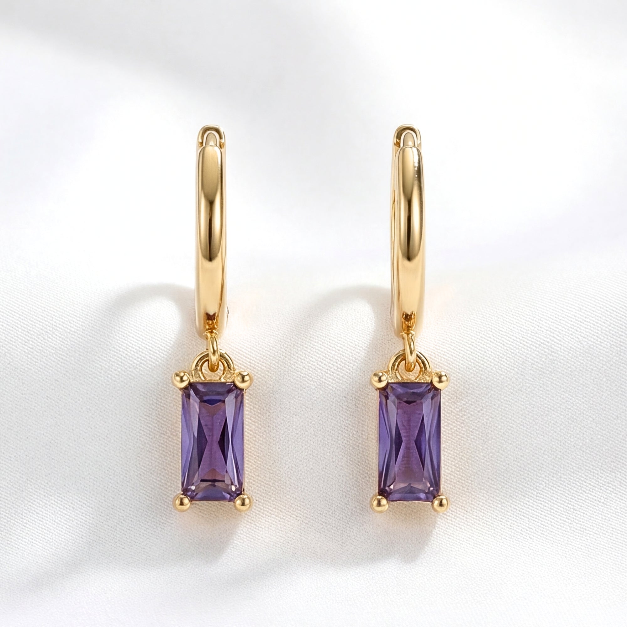 Front view of gold hoop earrings with emerald cut simulated amethyst drops on a white studio background.