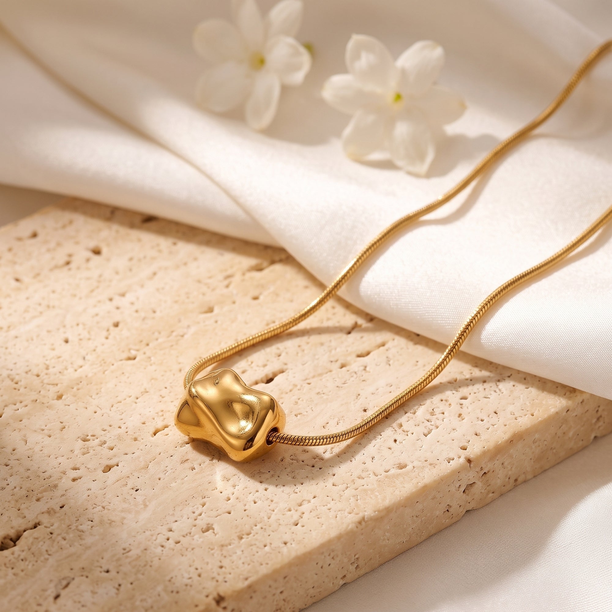 Close-up of the sculptural molten gold bead on a snake chain, resting on a textured stone surface.
