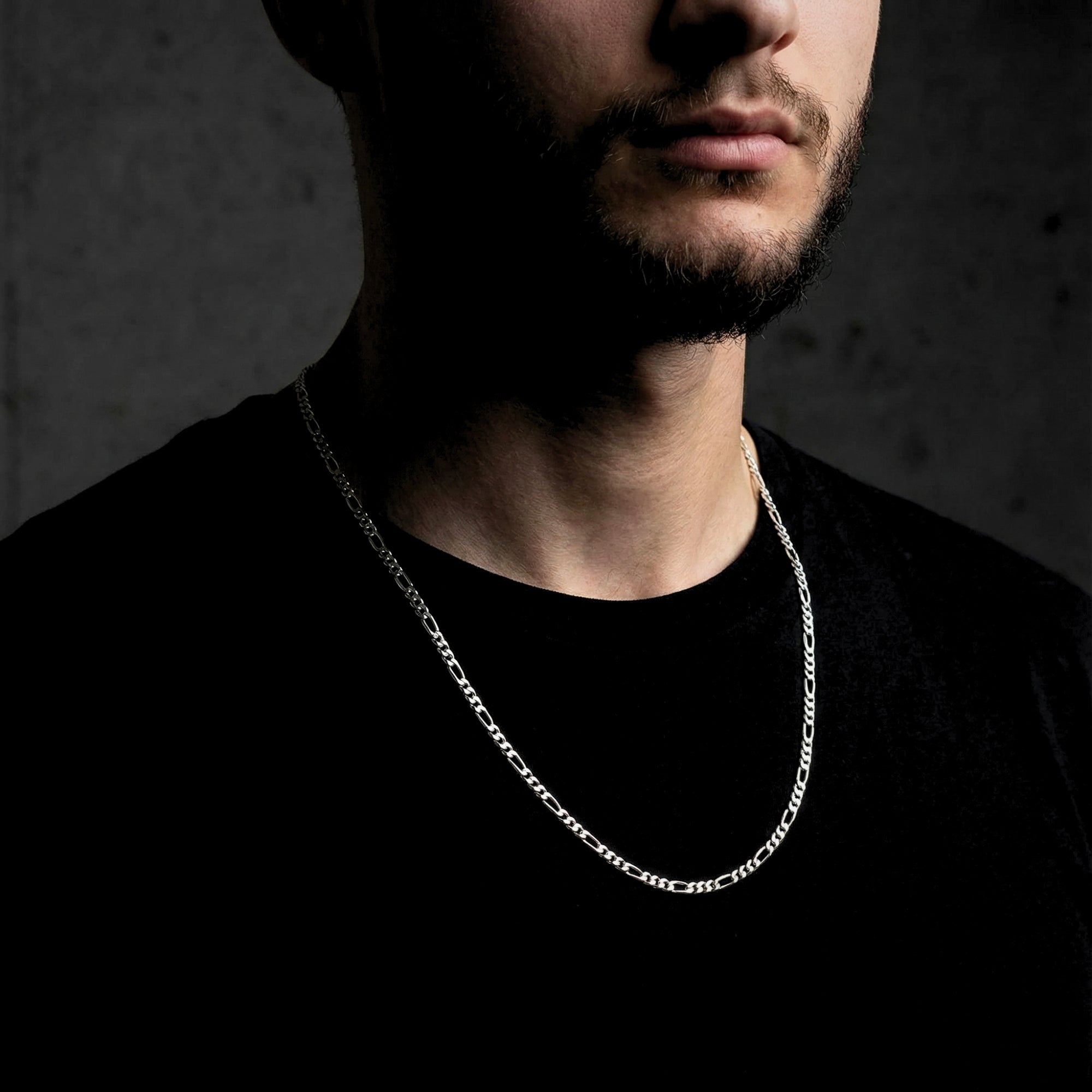 Men's 3mm silver stainless steel Figaro chain necklace worn by a model in a black shirt.