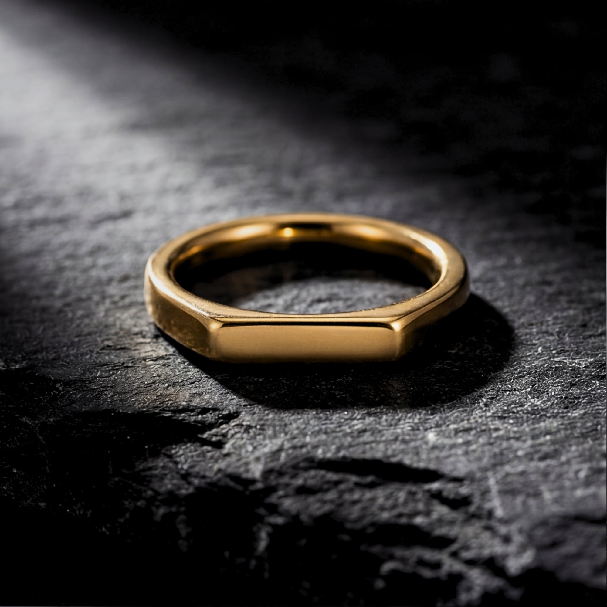 Front view of the gold stainless steel Pillar signet ring resting on a dark slate surface.