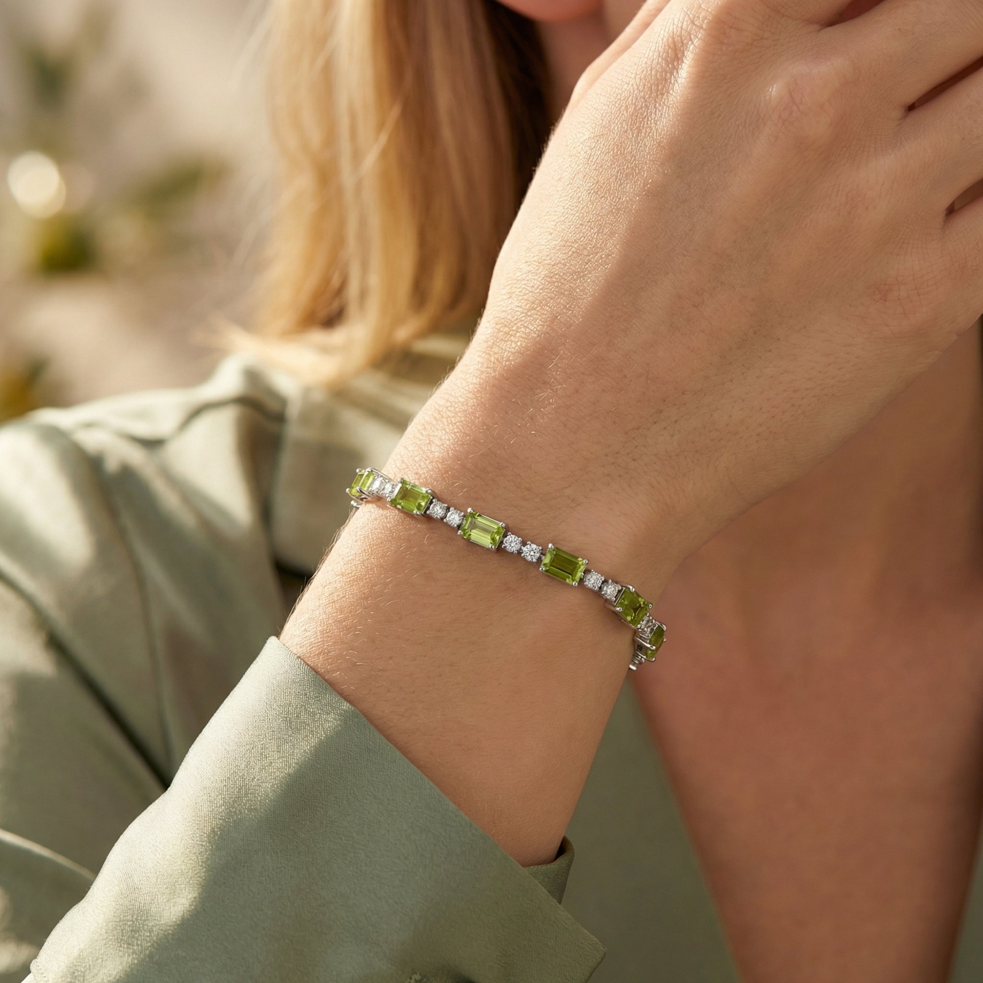 Close-up of the emerald cut peridot and sterling silver tennis bracelet worn on a woman's wrist.