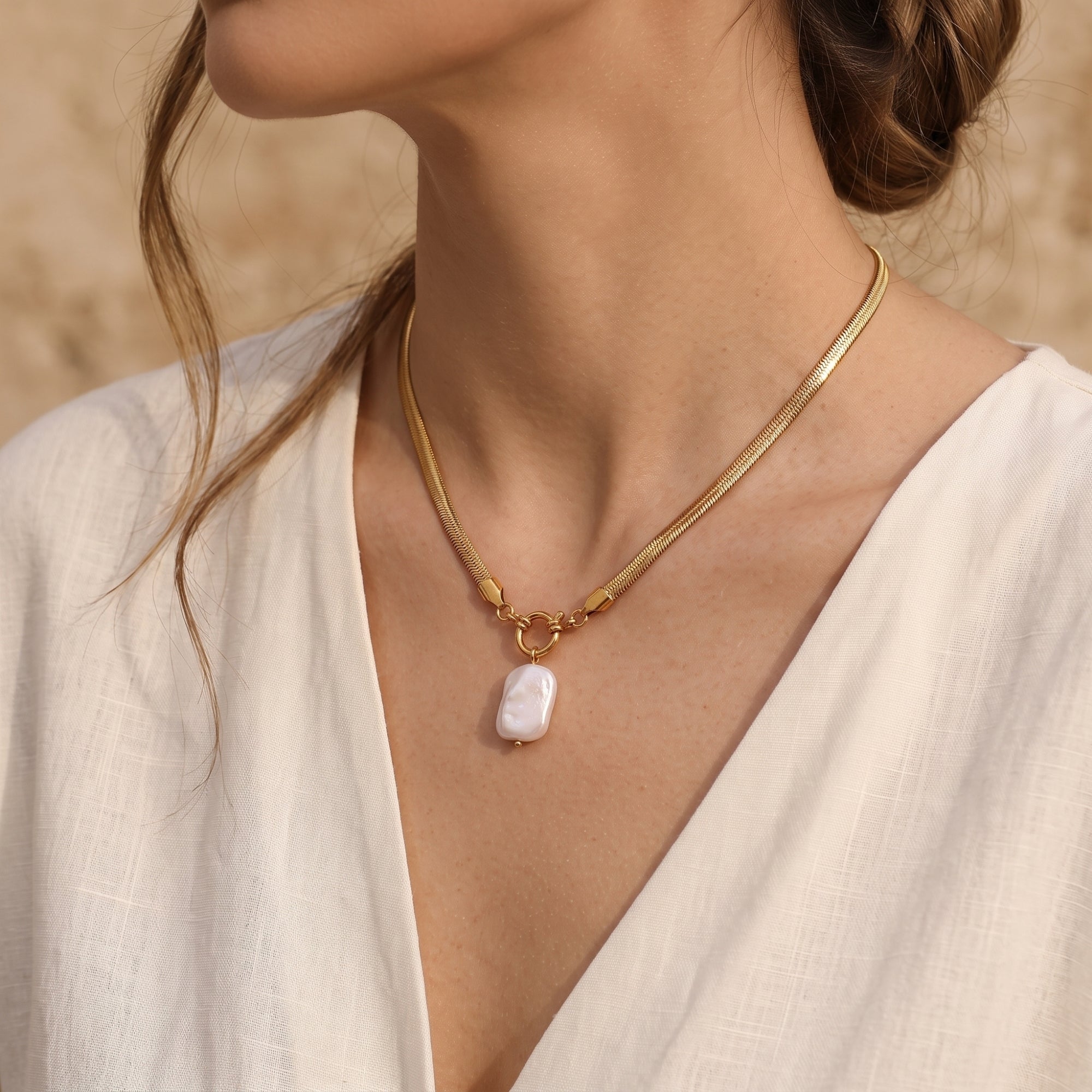 Side view of a model wearing the gold herringbone snake chain necklace with a white baroque pearl pendant.