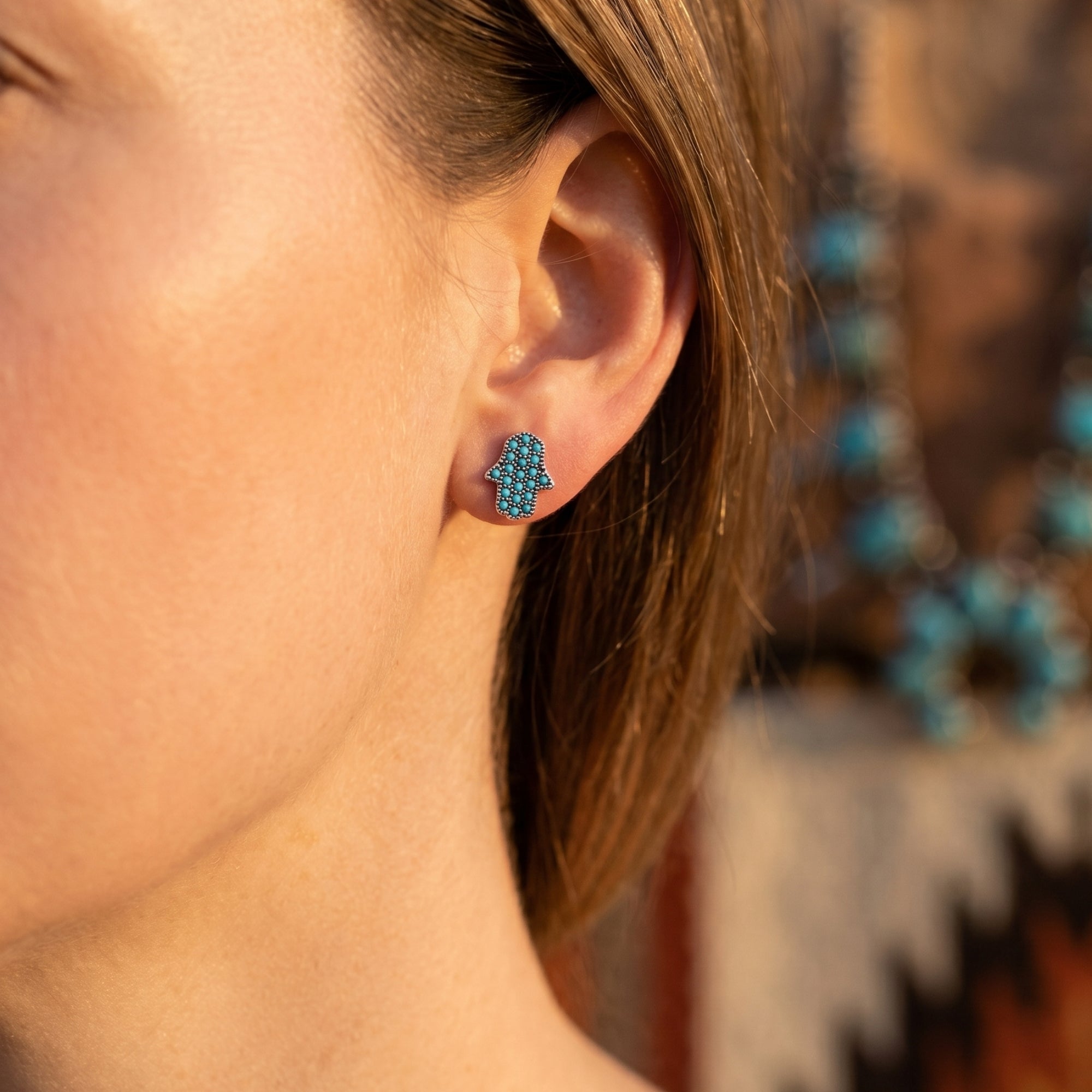 Side view of a silver Hamsa hand stud earring with turquoise stones worn on a woman's ear.