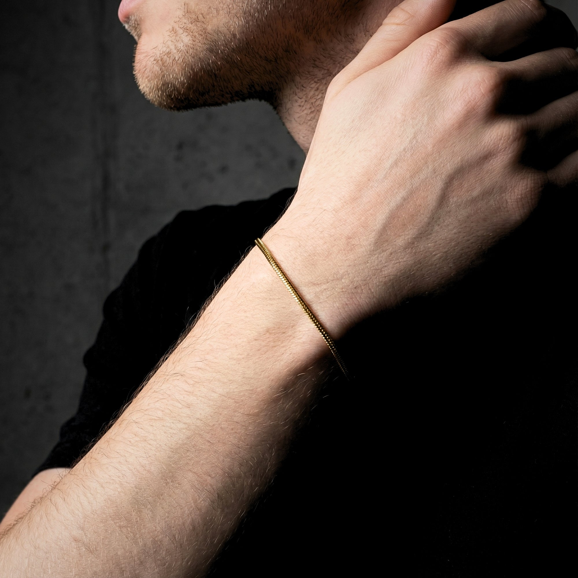 Side view of a gold-tone stainless steel square link bracelet worn on a man's wrist against a dark background.