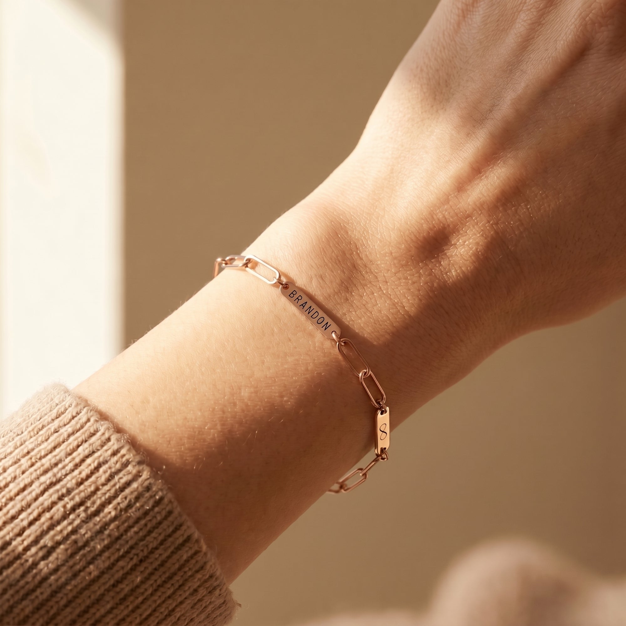 Rose gold personalized link bracelet with engraved name plate BRANDON worn on a wrist.