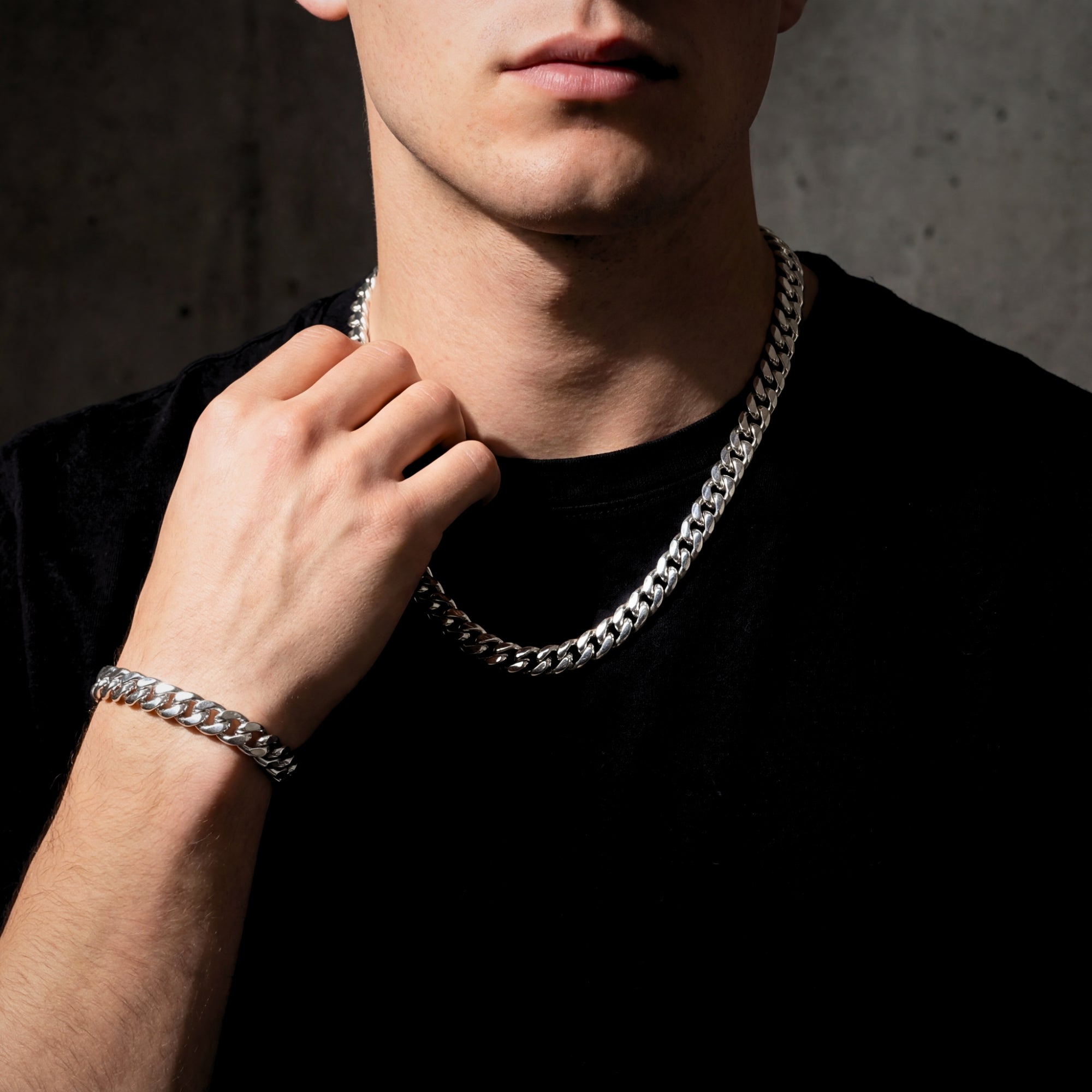 Man wearing the 10mm polished silver stainless steel Cuban link chain and bracelet set, hand near his neck.