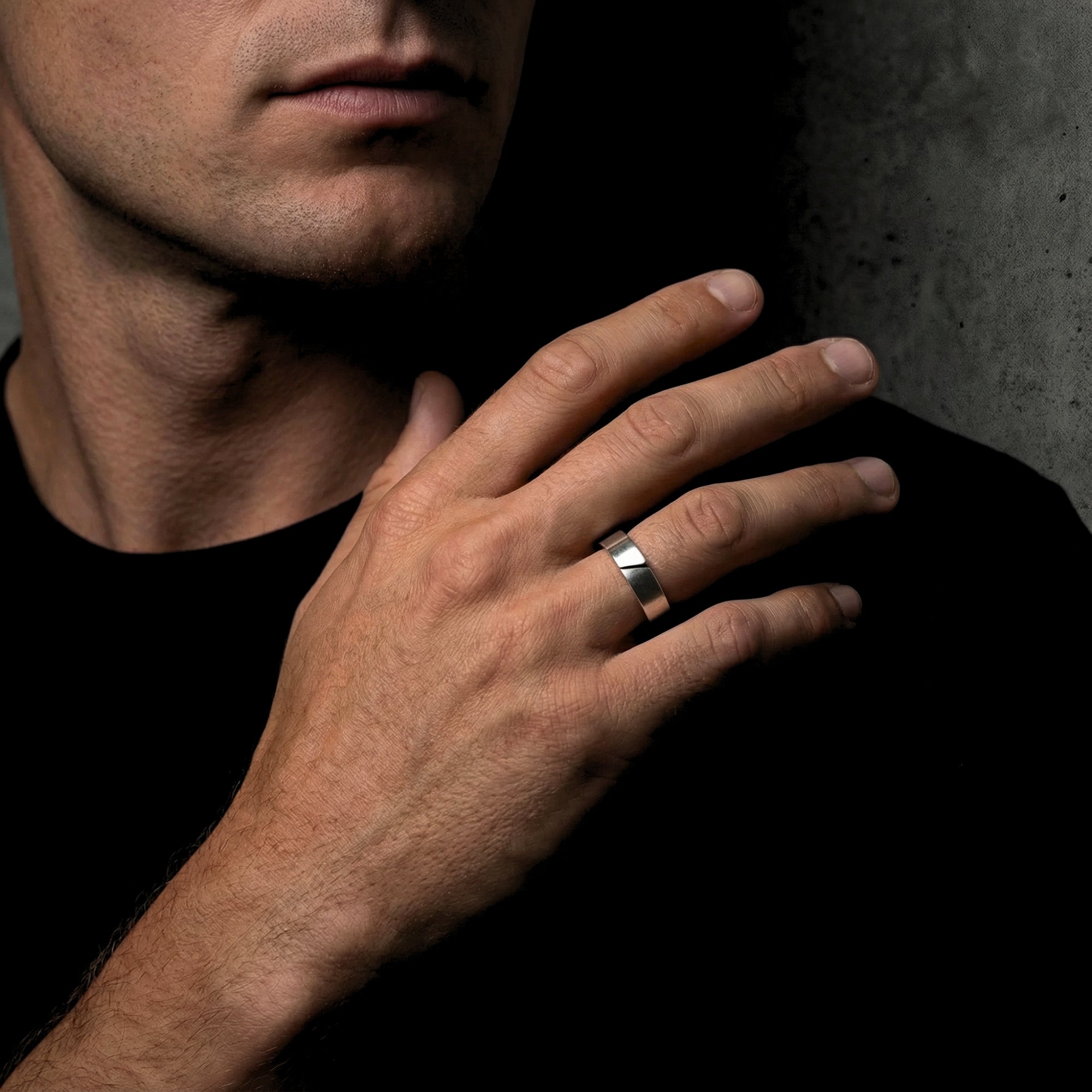 Brushed silver stainless steel Spartan band ring for men, shown on a hand in a lifestyle studio setting.