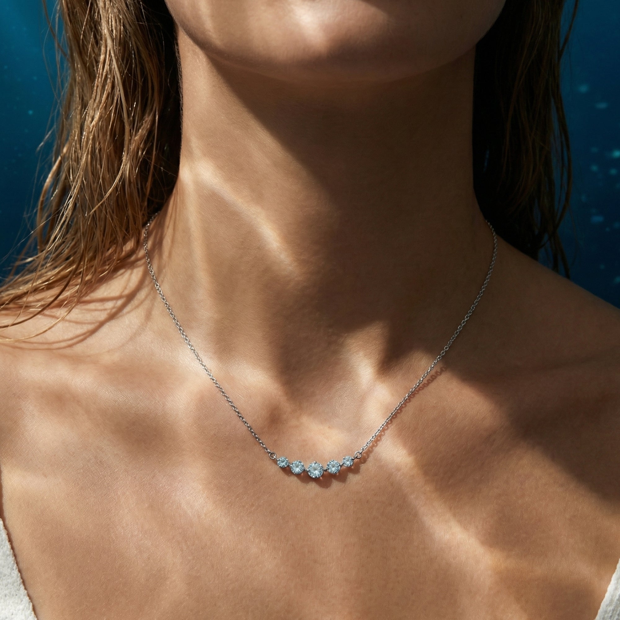 Model wearing the Ephyra platinum necklace featuring five graduated round cut aquamarine stones.