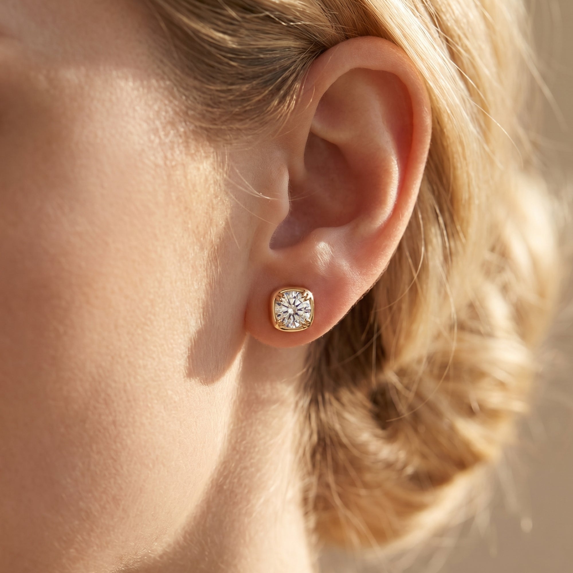 Gold Gabriella cushion-halo moissanite stud earring worn on a woman's ear.