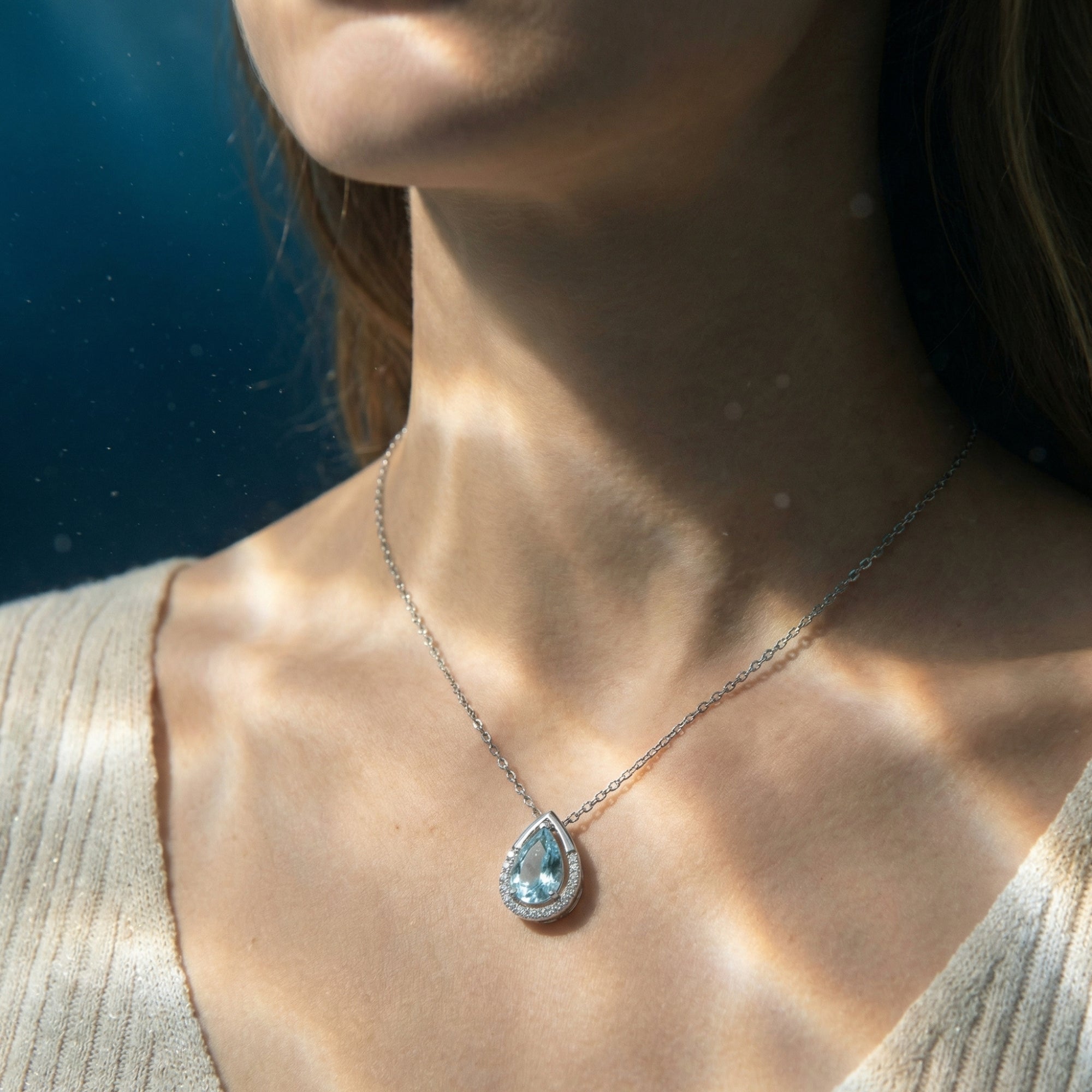 Model wearing the Lorelia pear cut aquamarine necklace in 18K white gold, featuring a diamond halo and chain.