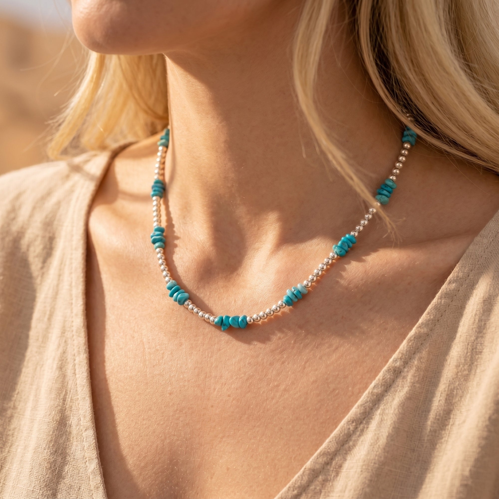 Model wearing the silver and turquoise bead necklace with a beige linen top in natural sunlight.