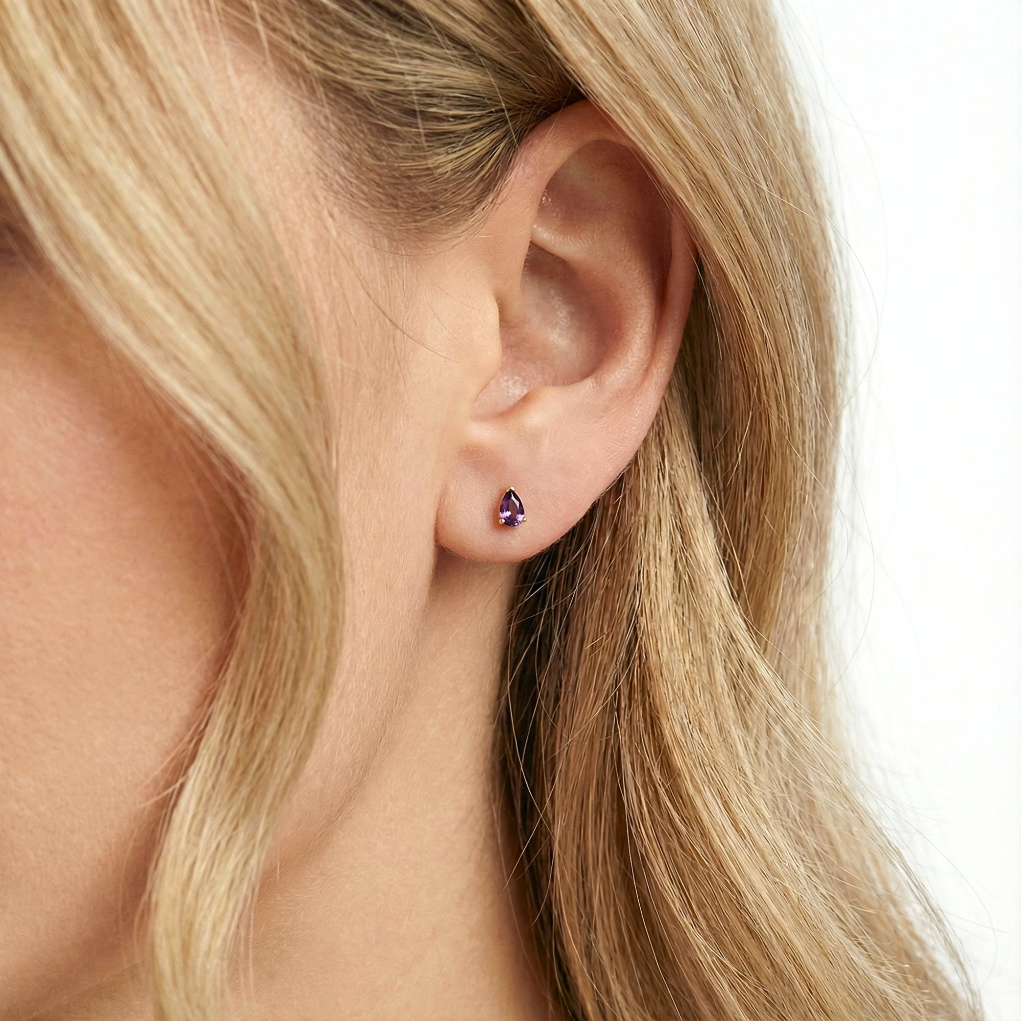 Close-up of a purple teardrop simulated amethyst gold vermeil stud earring worn on a model's ear.