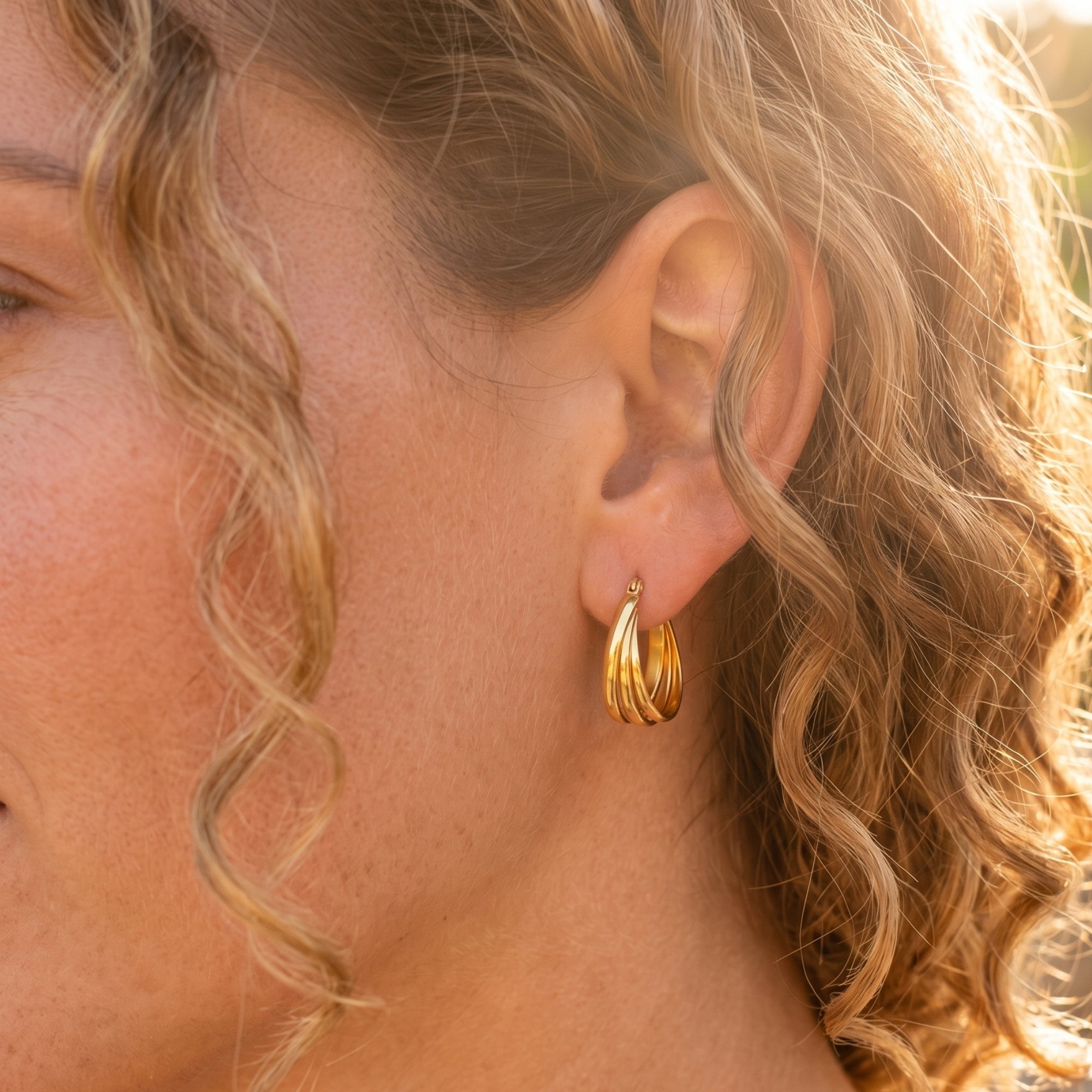 Side view of a woman wearing gold triple-row woven hoop earrings.