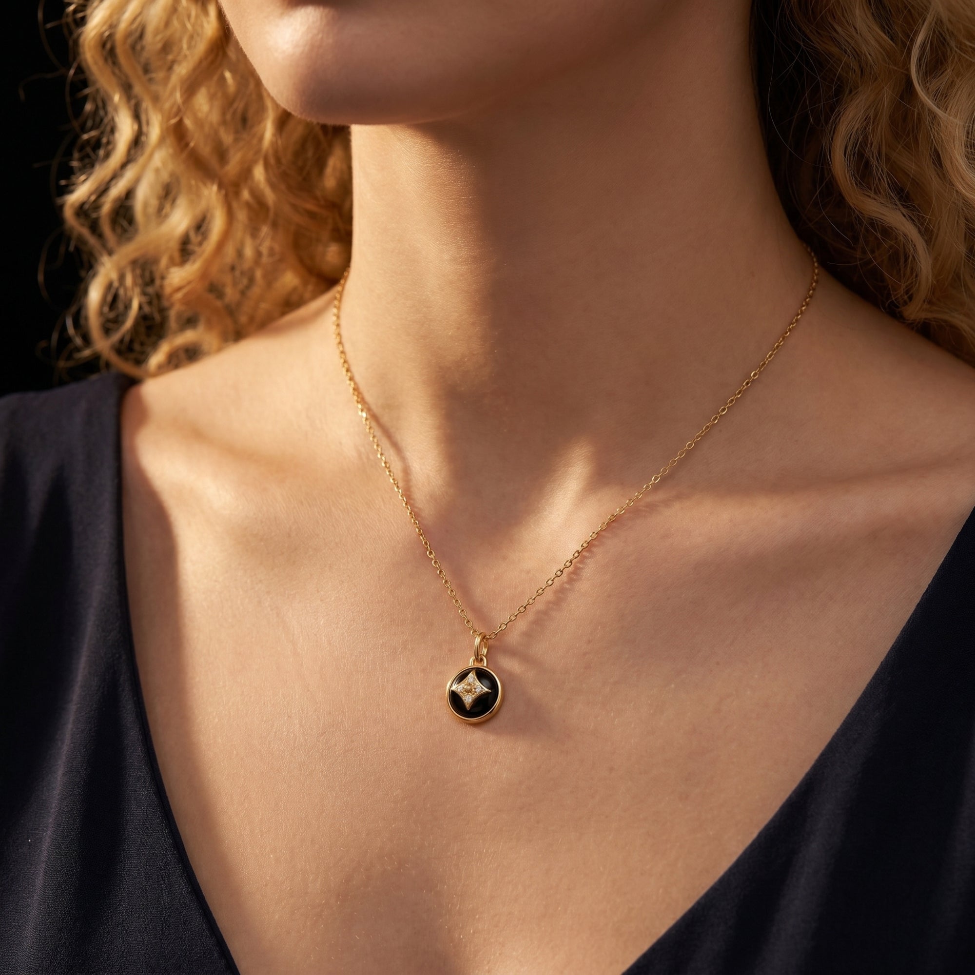 Gold plated Equinox natural onyx pendant necklace worn by a model with curly hair and a black top.