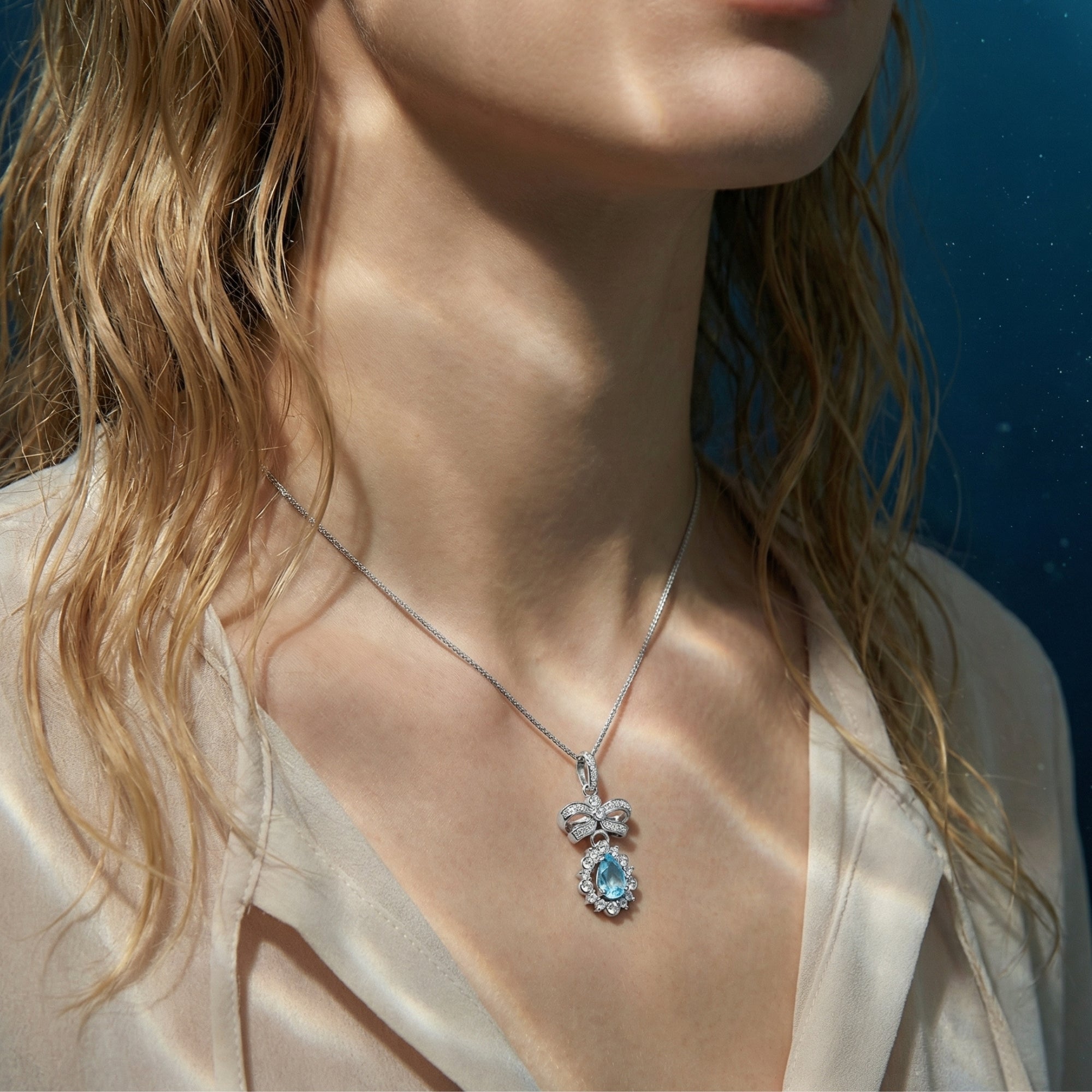 Silver pear cut aquamarine necklace with a bow pendant worn by a model, showcasing its fit against the collarbone.