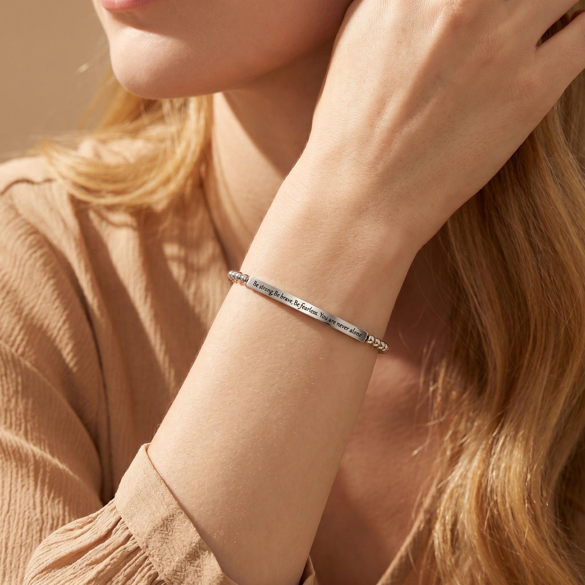 Silver engraved bar bracelet with beaded chain worn on a woman's wrist.