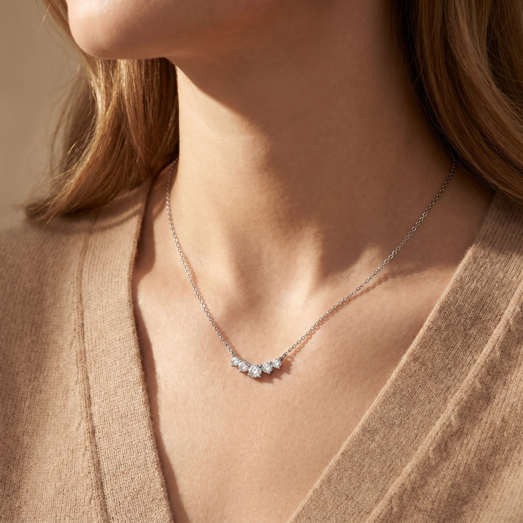 Model wearing the silver Antonella moissanite smile necklace against a tan cardigan.