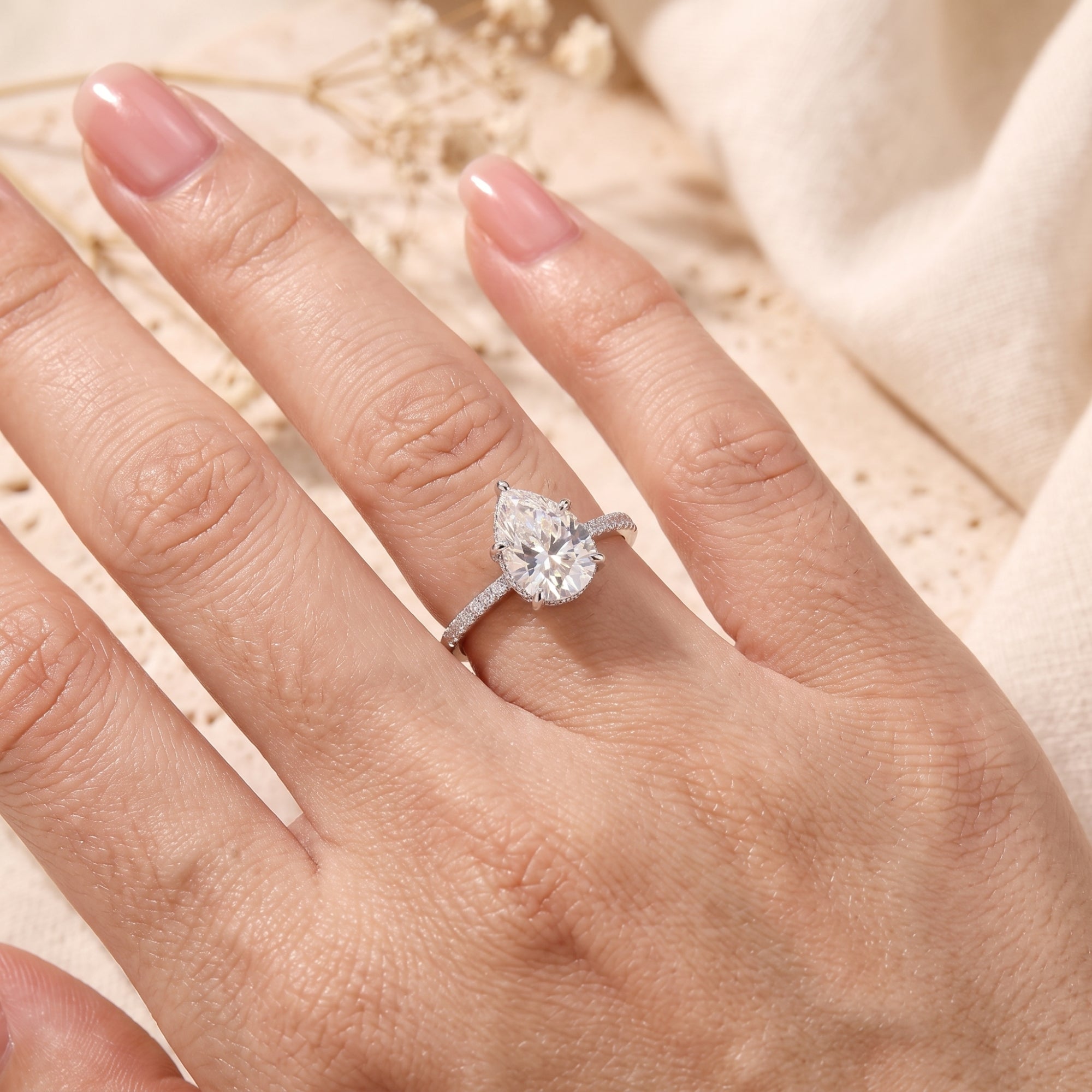 Close-up of a pear-cut simulated diamond sterling silver ring on a hand with a lifestyle background.