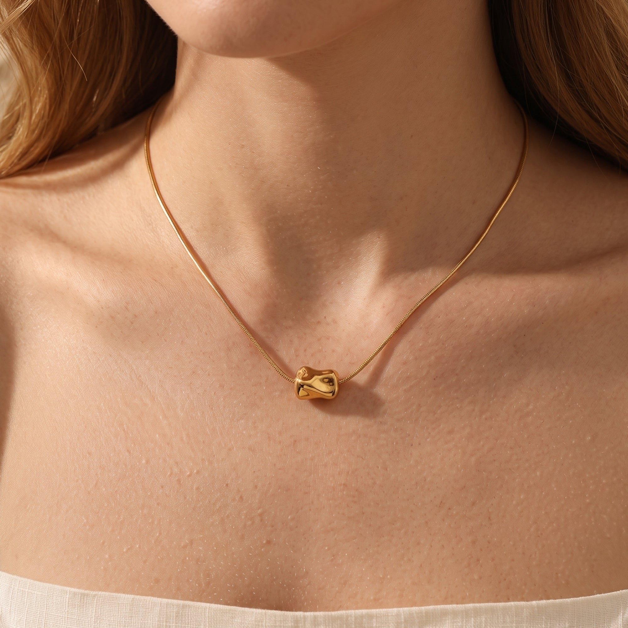 Front view of the 18K gold finish Petra necklace with a molten sculptural pendant worn by a model.