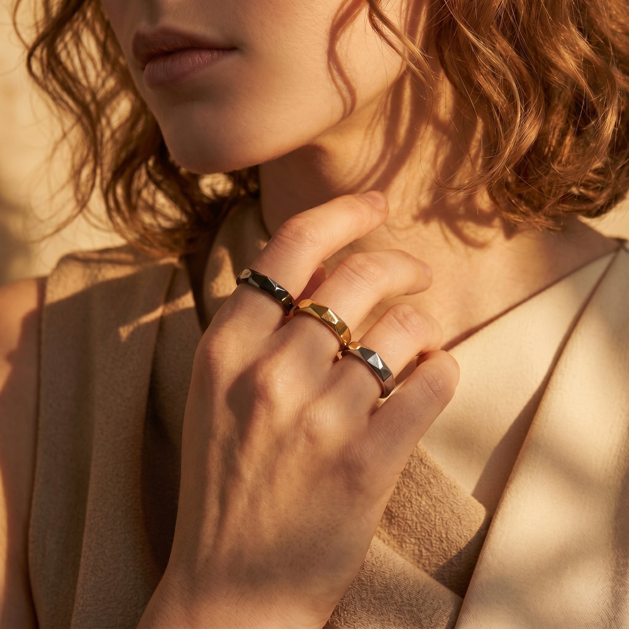 Three faceted stainless steel rings styled across multiple fingers on a model's hand in warm light.